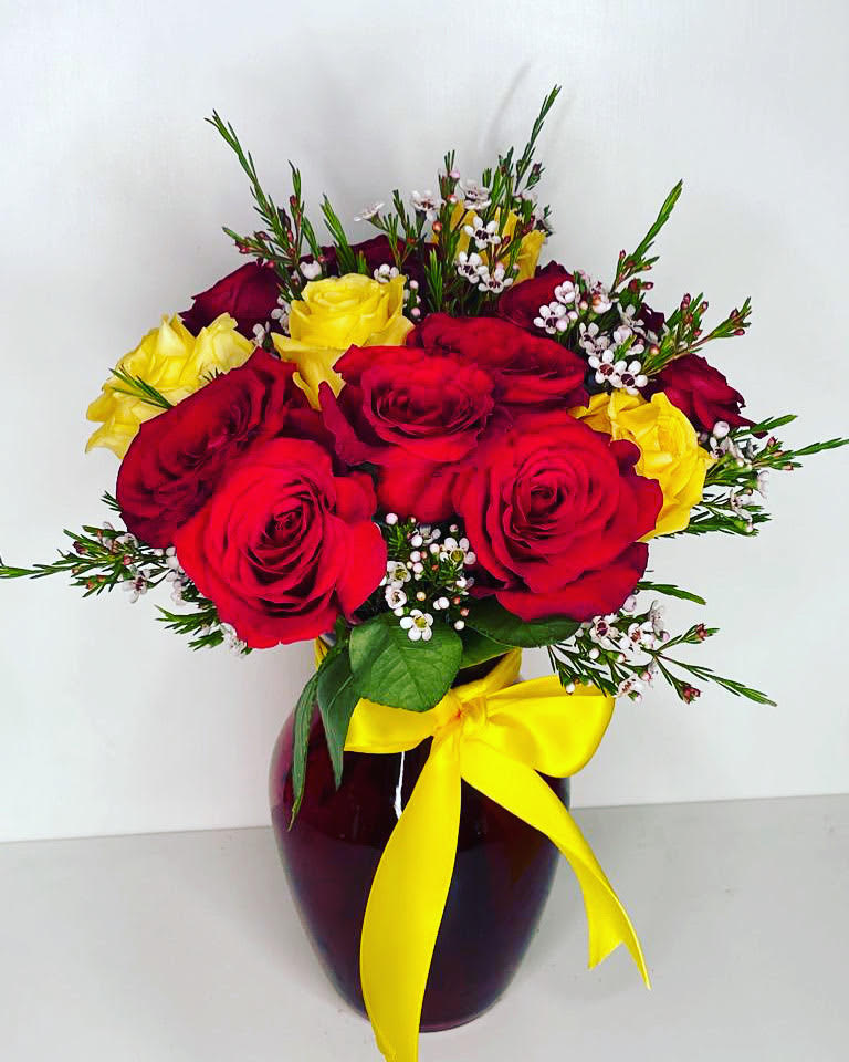 Red and yellow roses in a dark vase with a yellow ribbon