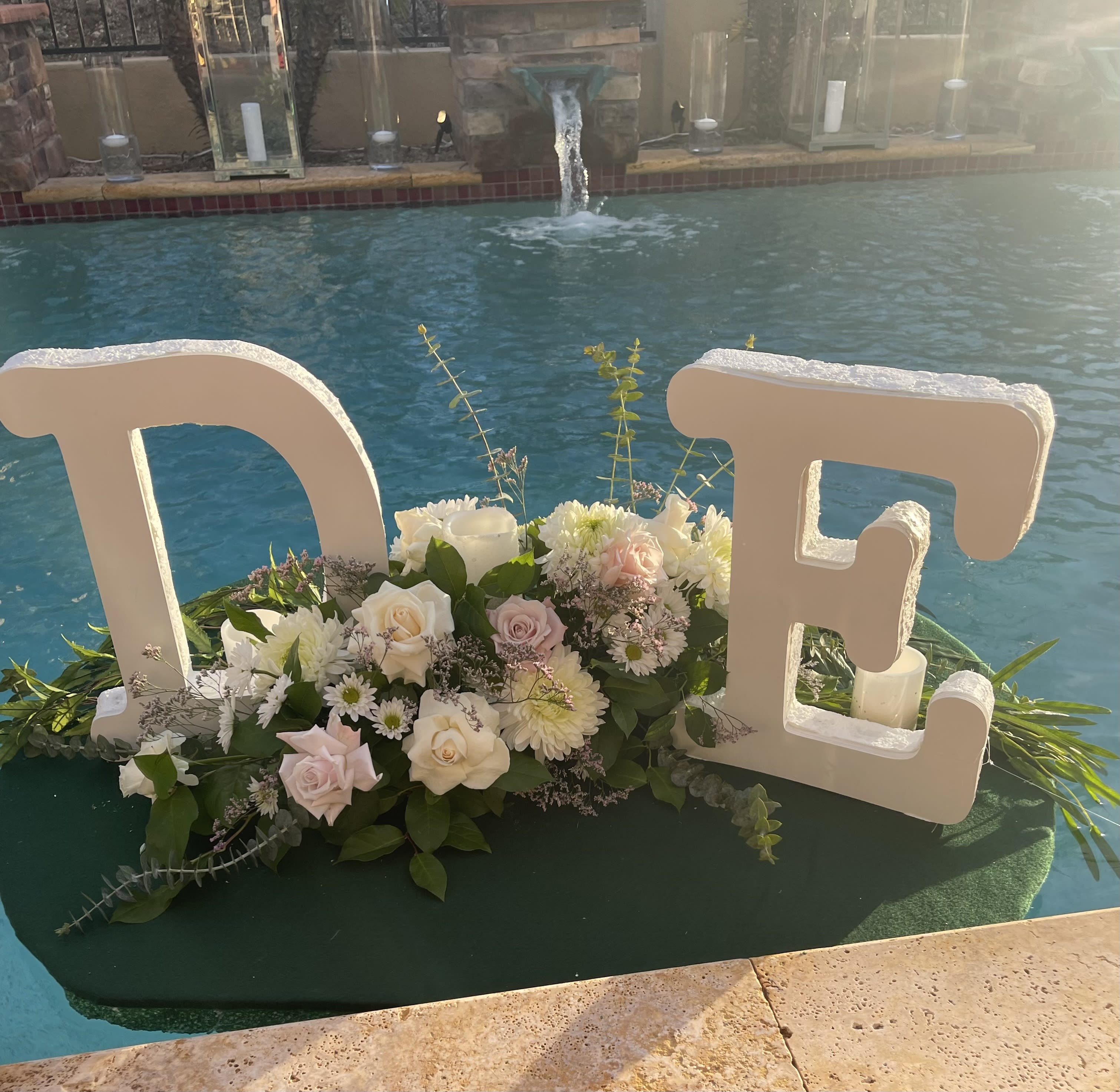 White floral arrangement with large letters spelling "TE" beside a pool