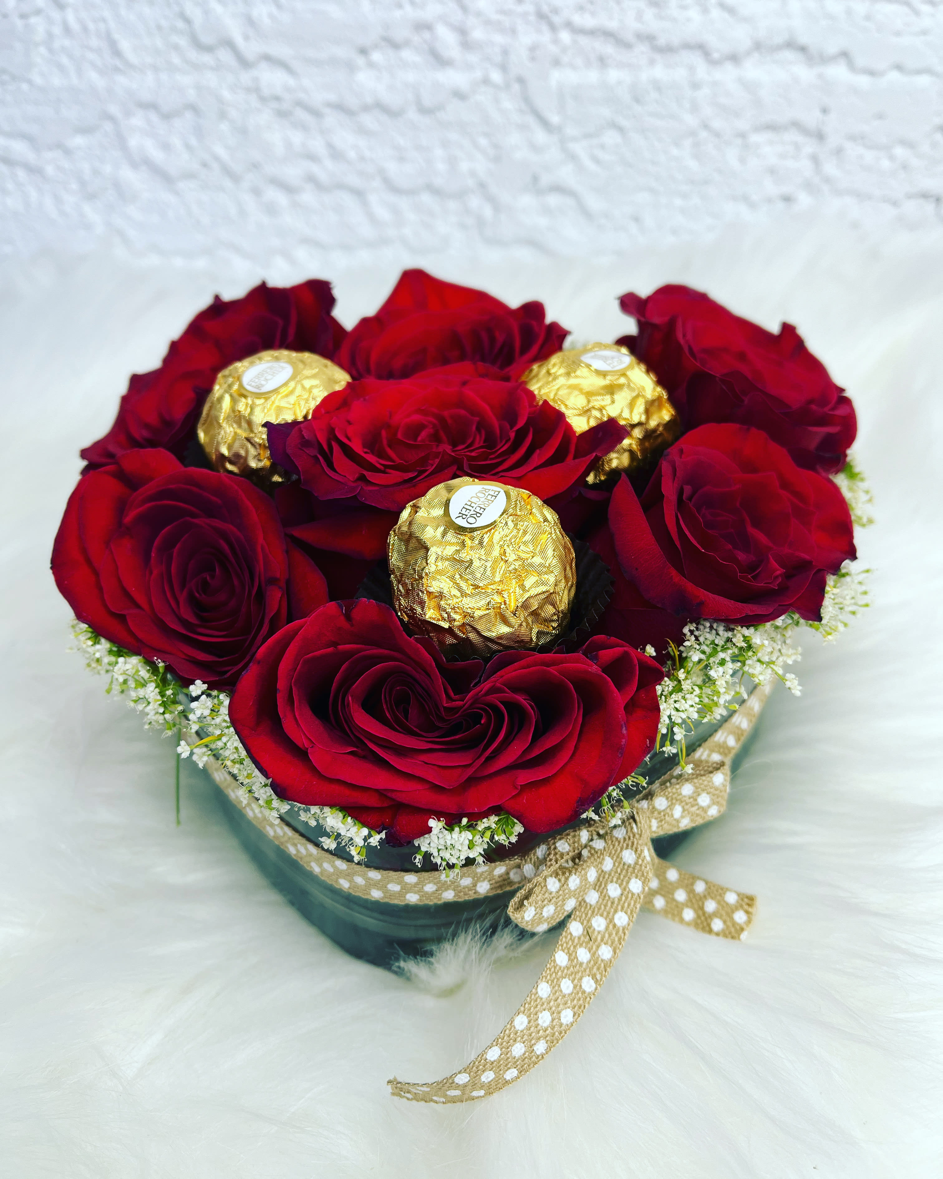 Red roses arranged with gold-wrapped chocolates in a round box