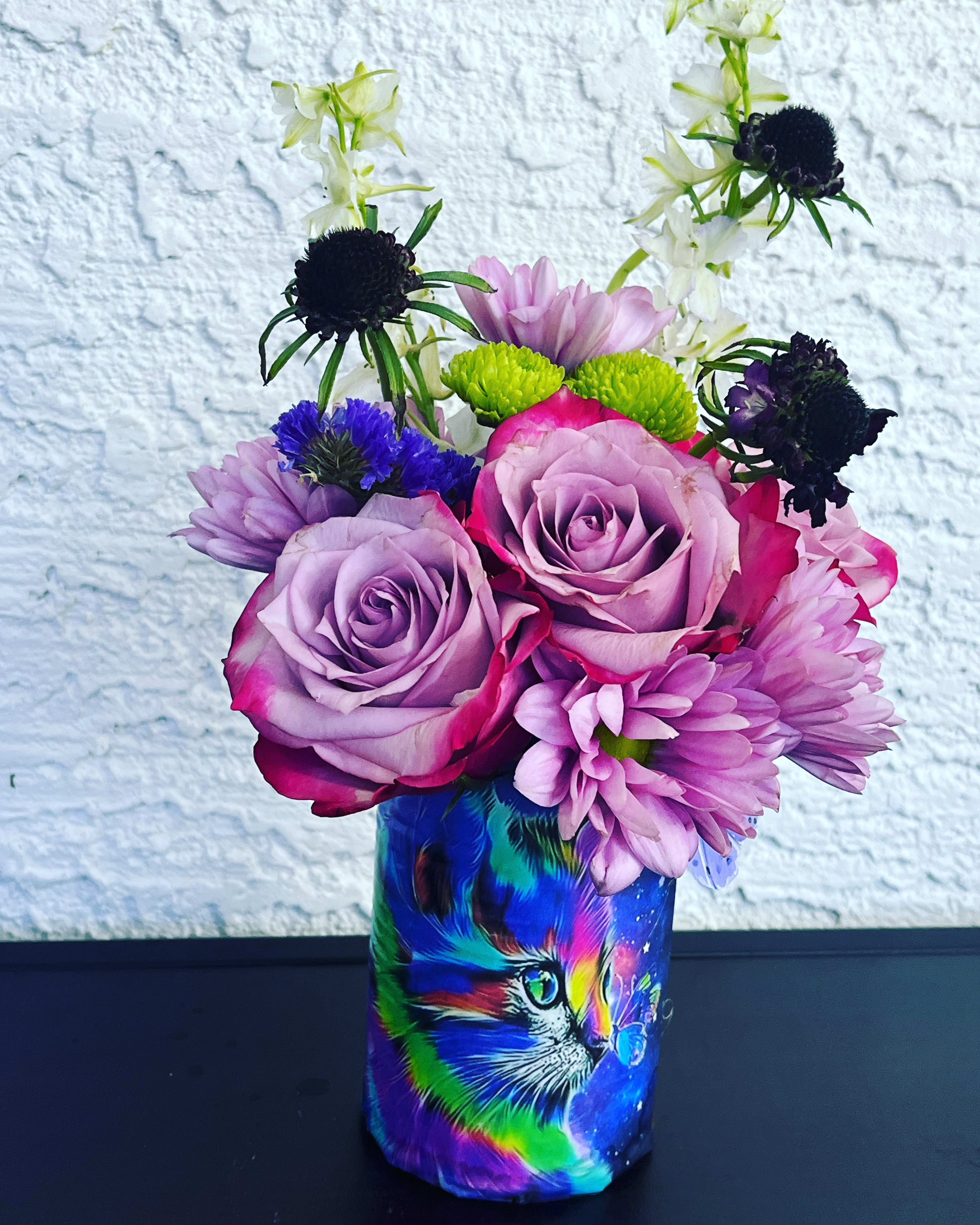 Bouquet of purple roses and mixed blooms in a colorful cat-print vase