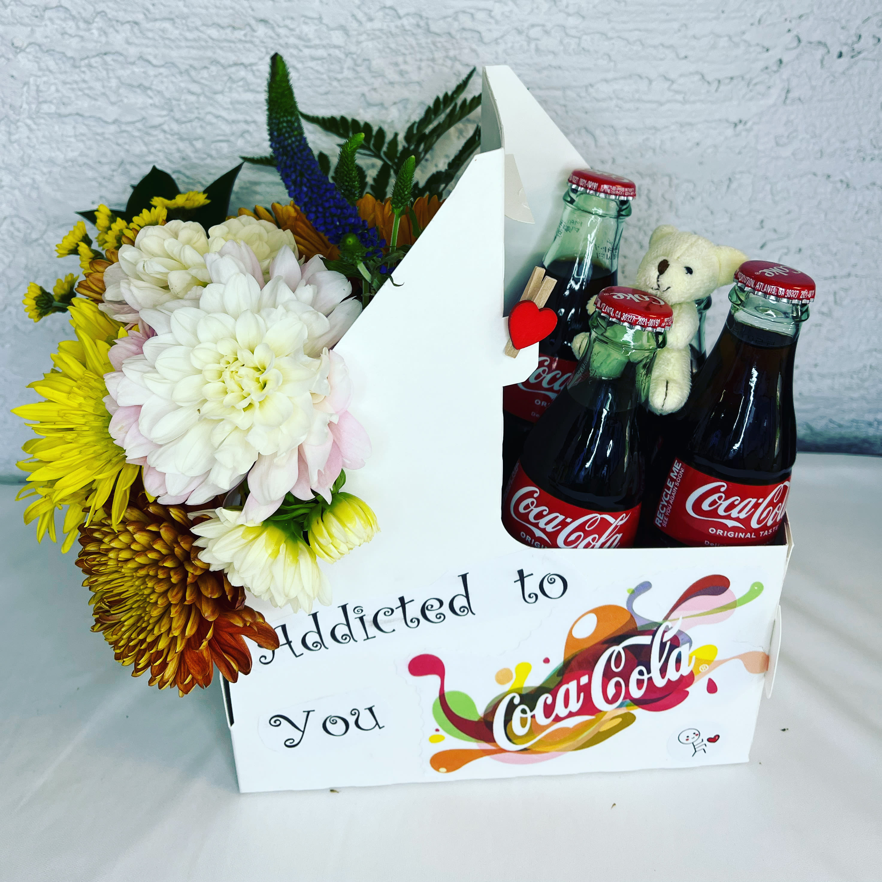 Flower arrangement with Coca-Cola bottles and a teddy bear in a gift box
