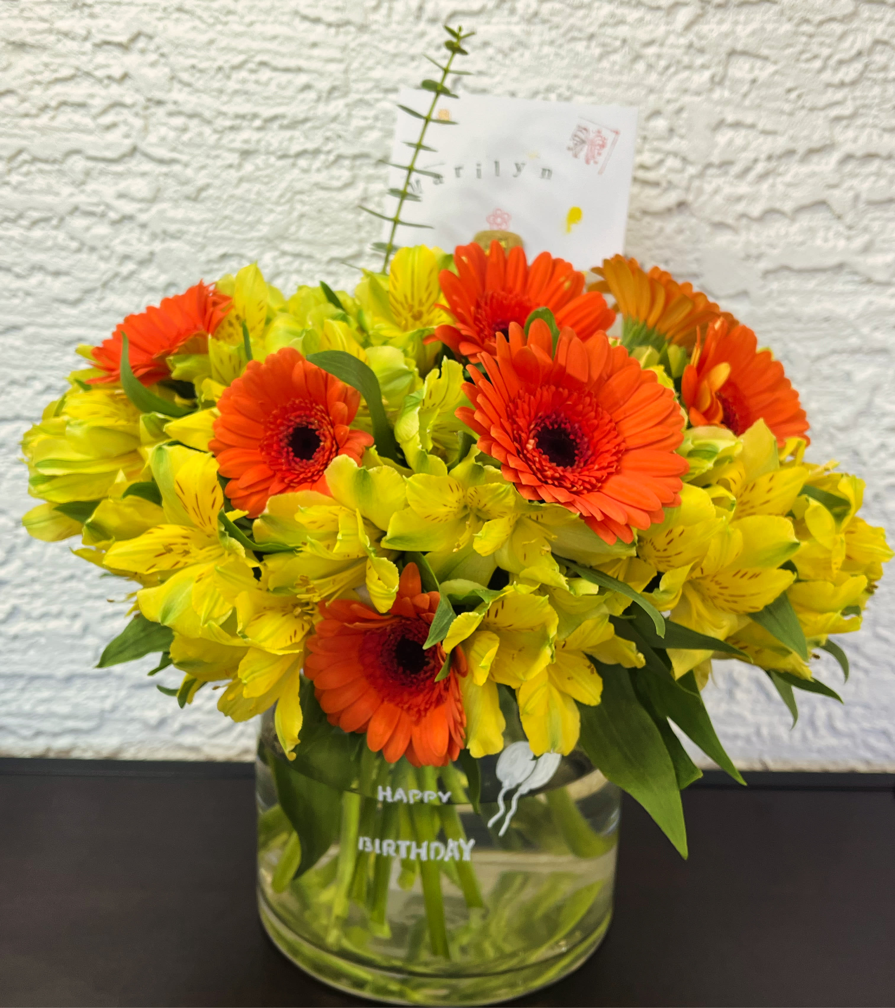 Orange gerbera daisies and yellow alstroemeria in a glass vase