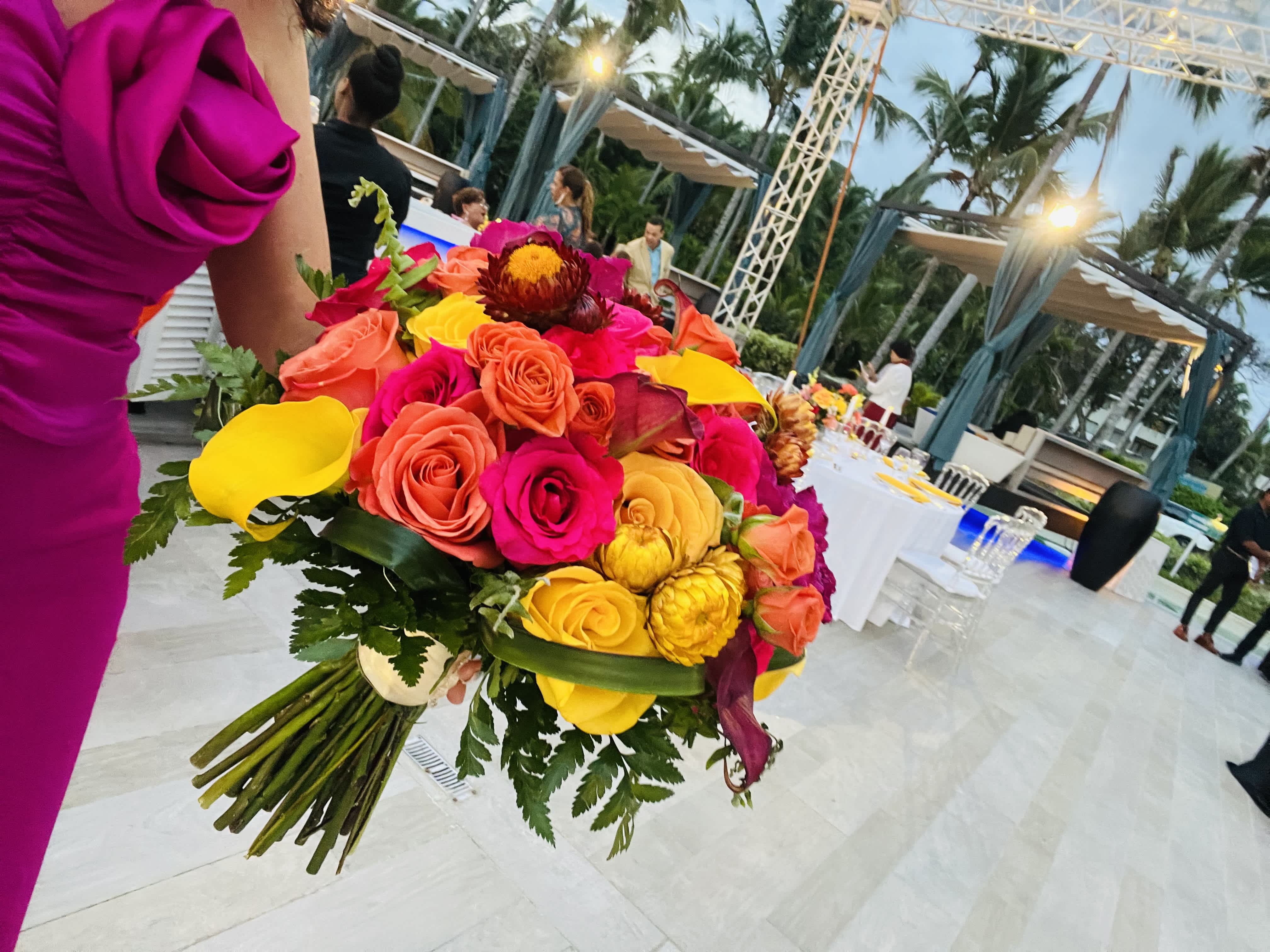 Bright bouquet of roses and calla lilies held at an outdoor event.