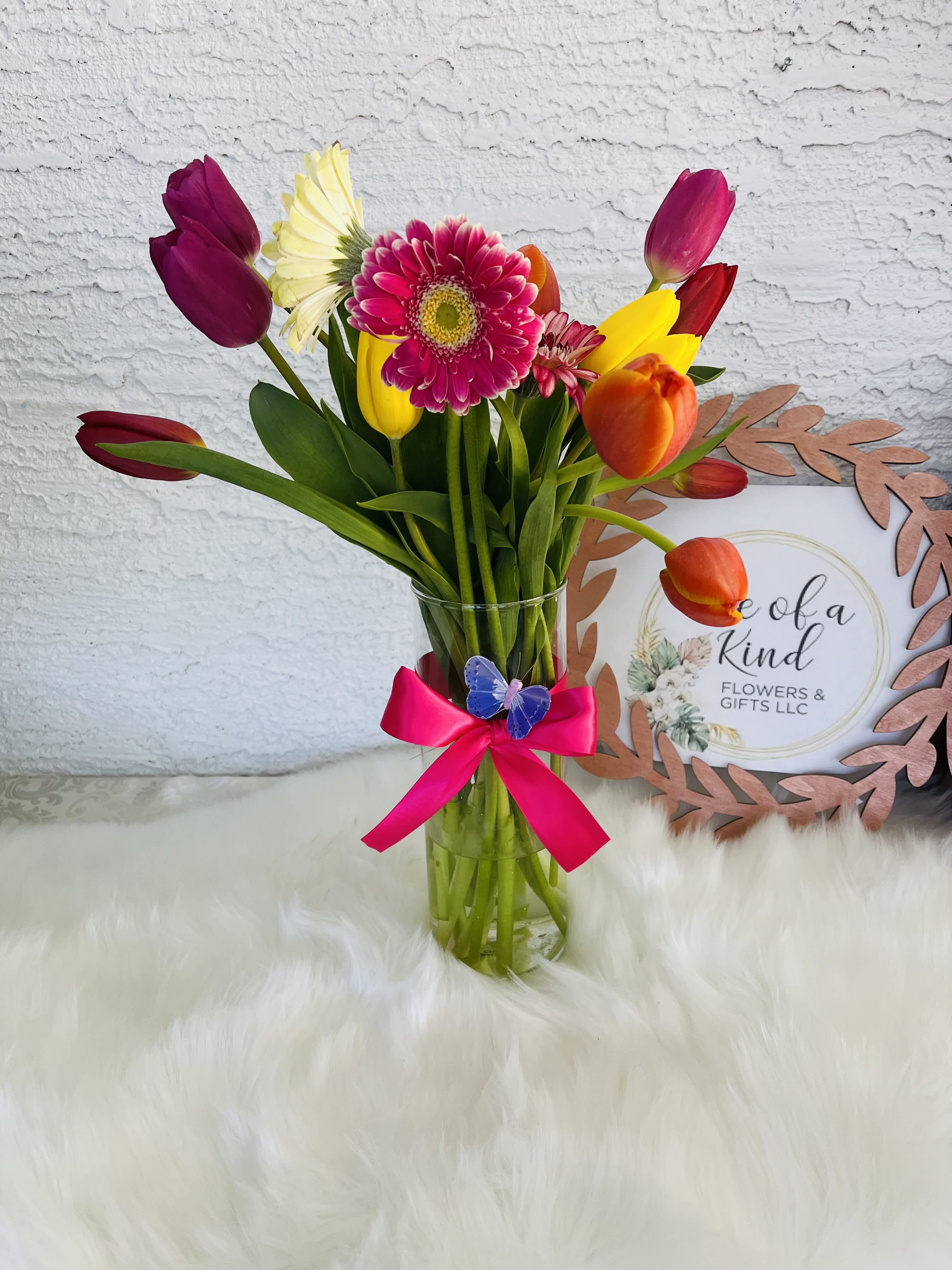 Colorful tulip and gerbera bouquet in a clear glass vase with a pink ribbon