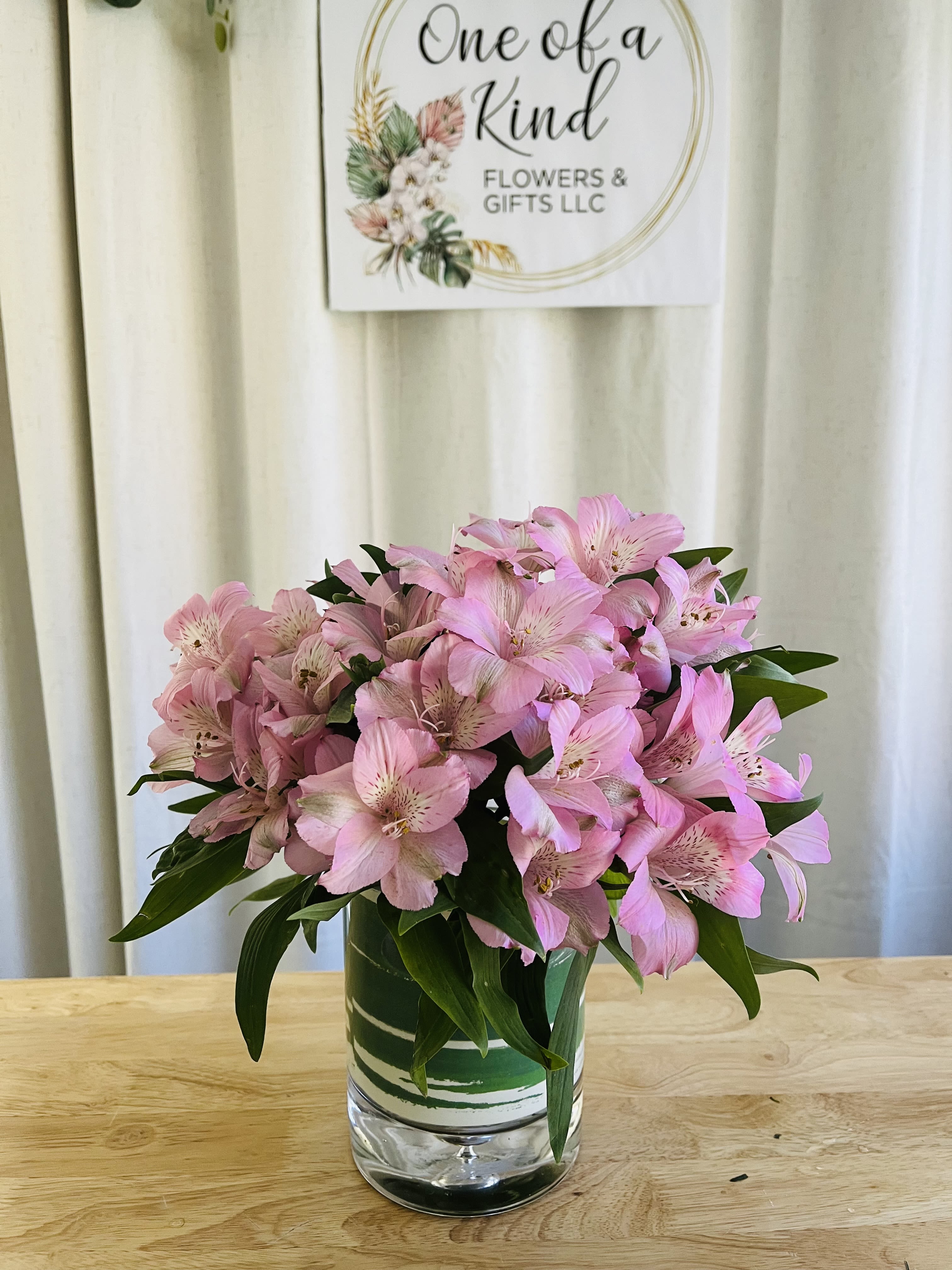 Compact bouquet of pink alstroemeria in a clear glass cylinder vase on a wooden table.
