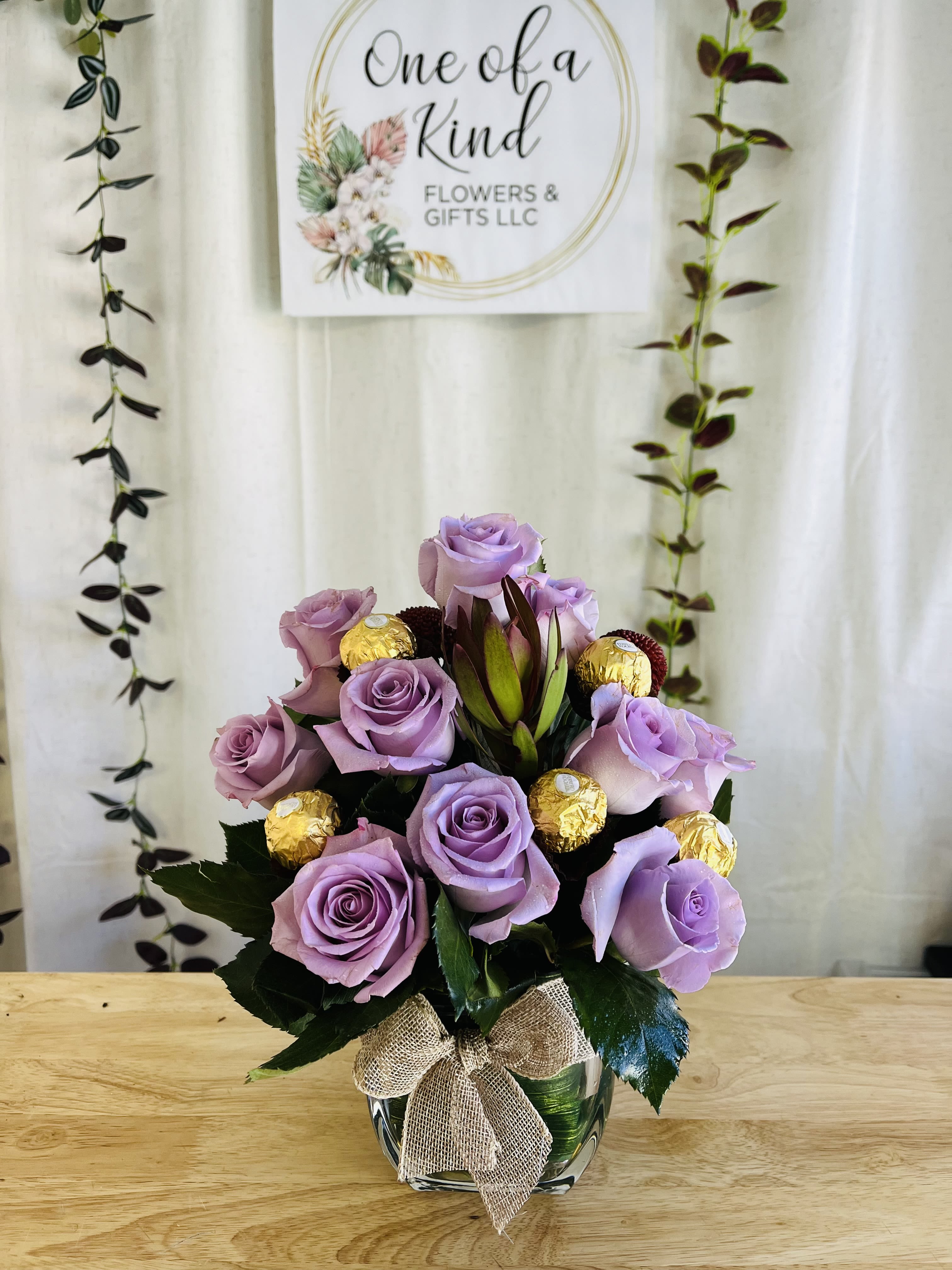 Lavender rose arrangement in a glass vase with gold-wrapped chocolates