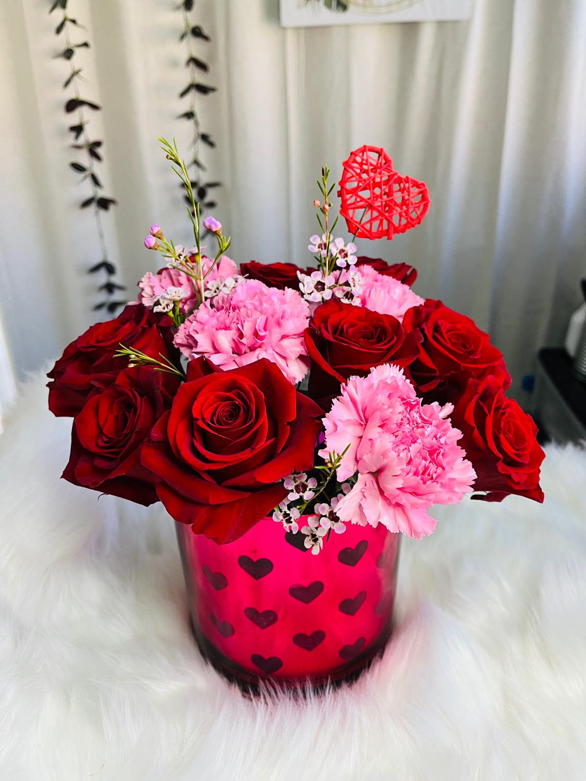 Red roses and pink carnations in a heart-decorated vase with a red heart pick