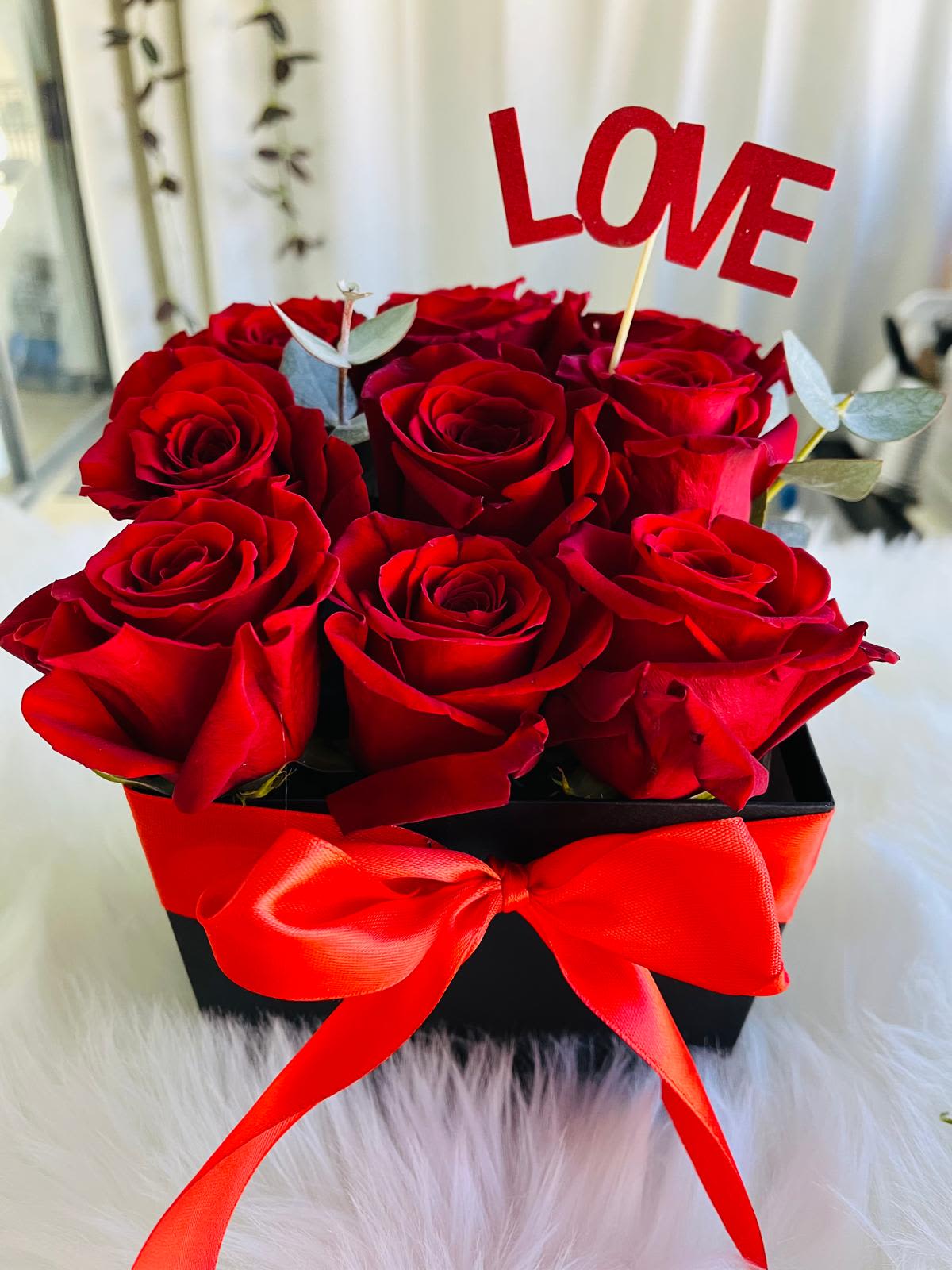 Red roses in a black box with a red ribbon and LOVE topper