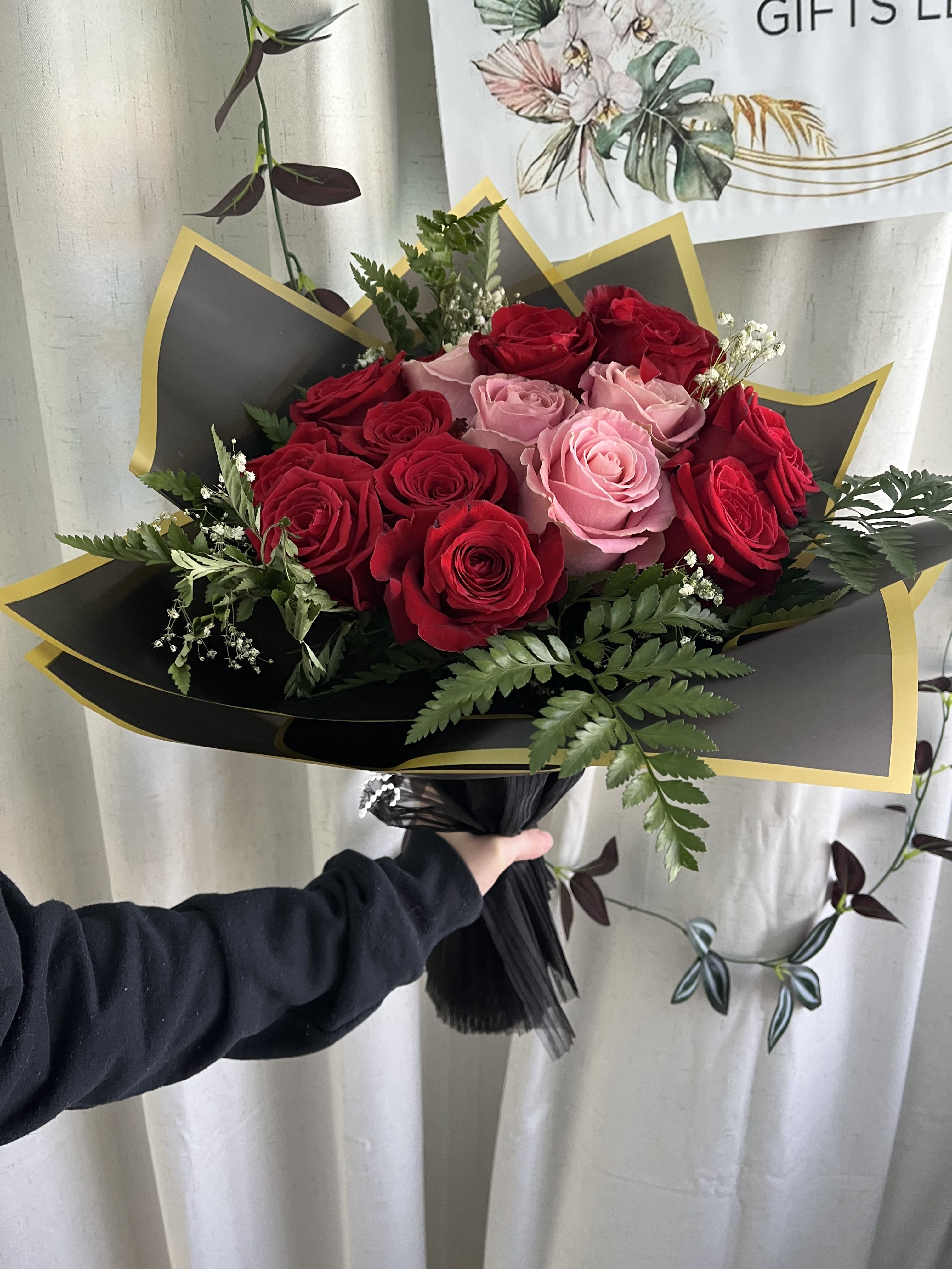 Bouquet of red and pink roses wrapped in black paper with gold trim