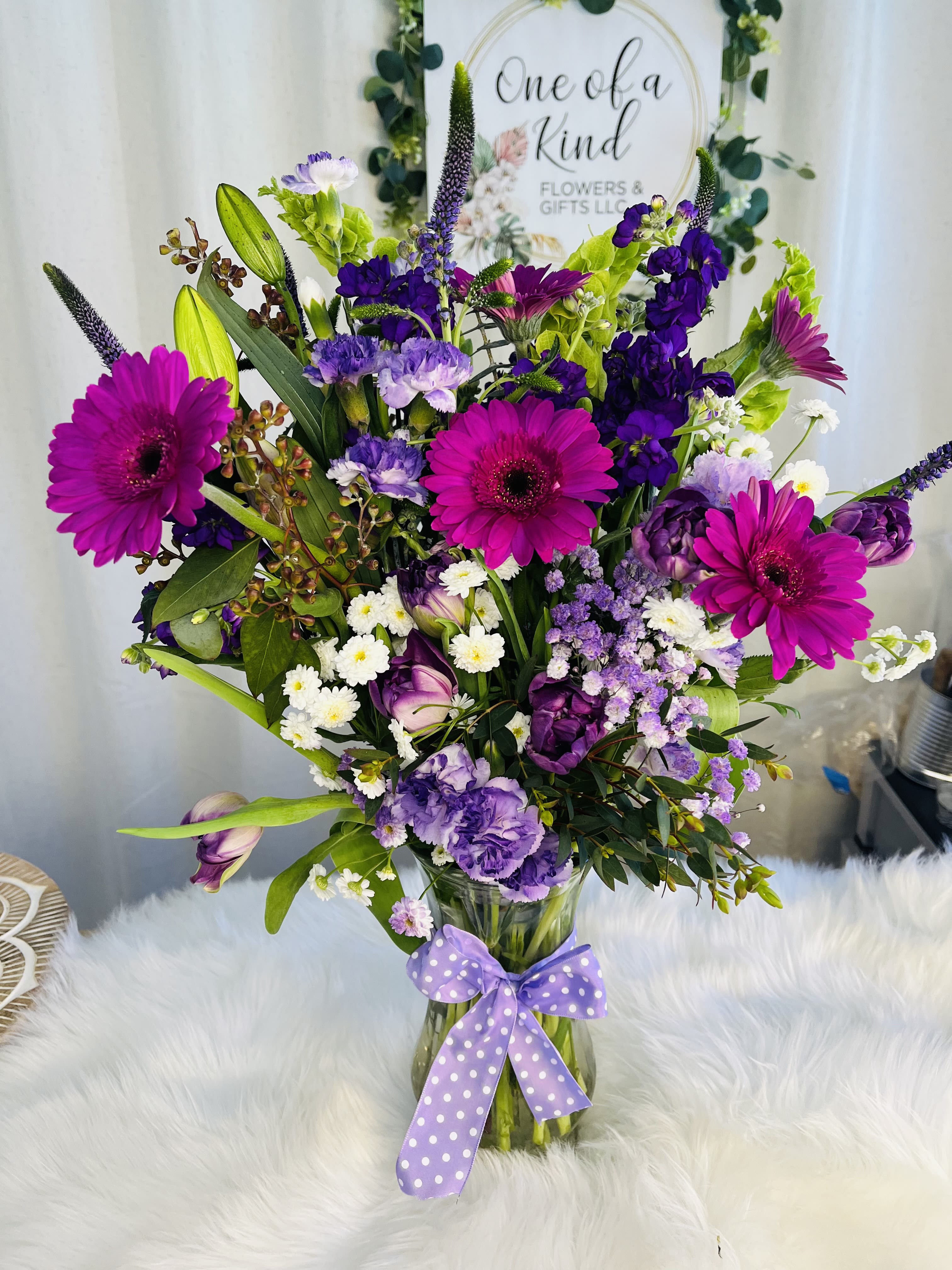 Mixed purple and pink bouquet in a glass vase with a polka-dot ribbon