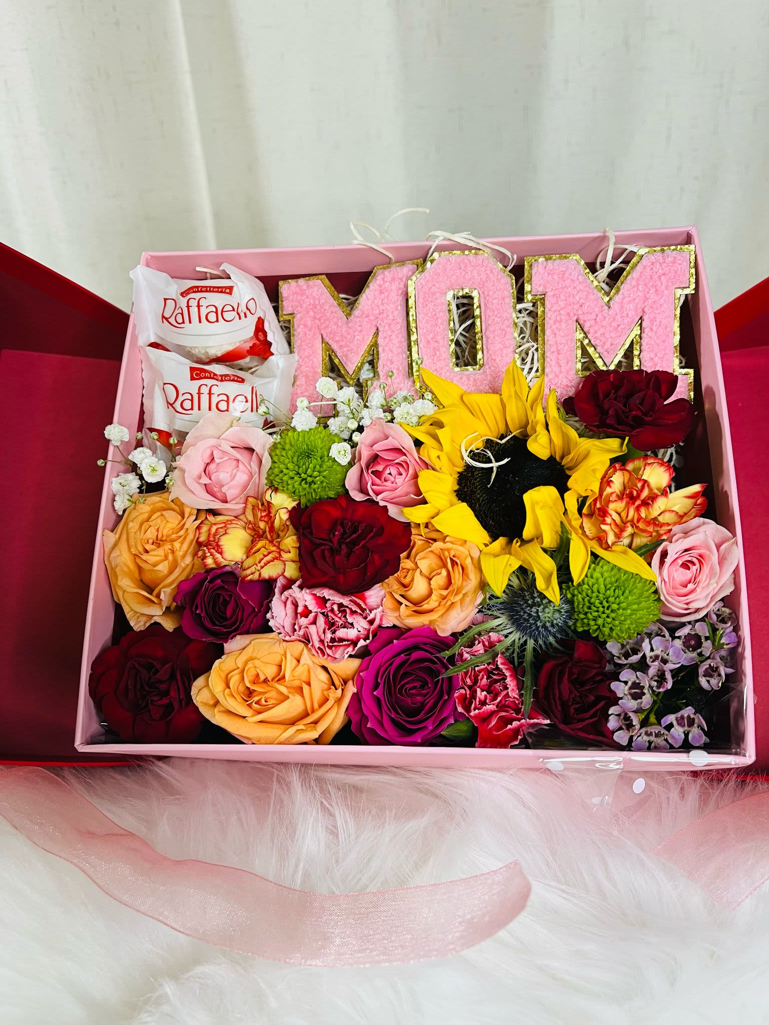 Gift box with pink MOM letters, roses, sunflowers, and chocolates