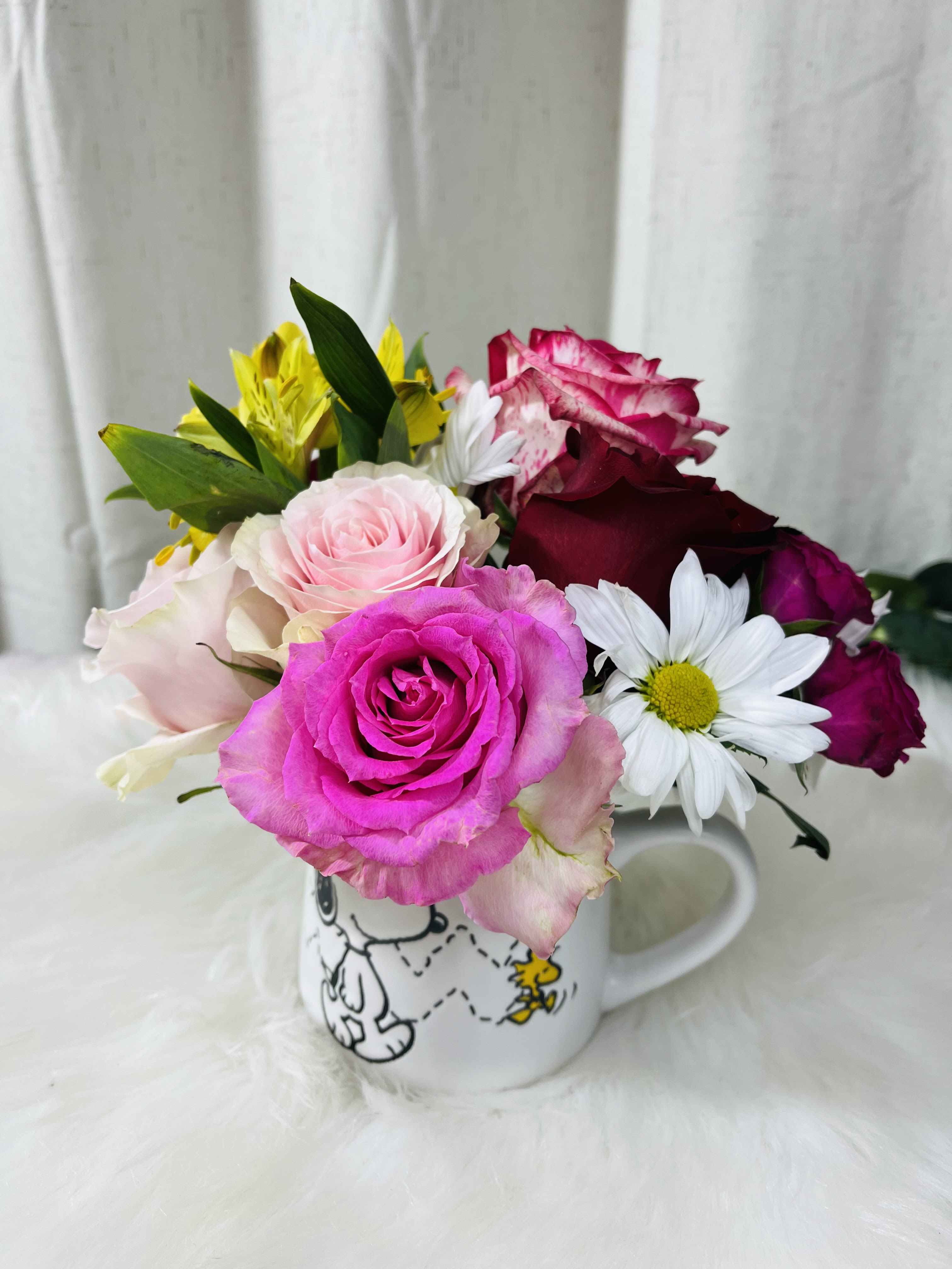 Mixed roses and daisies arranged in a Snoopy mug