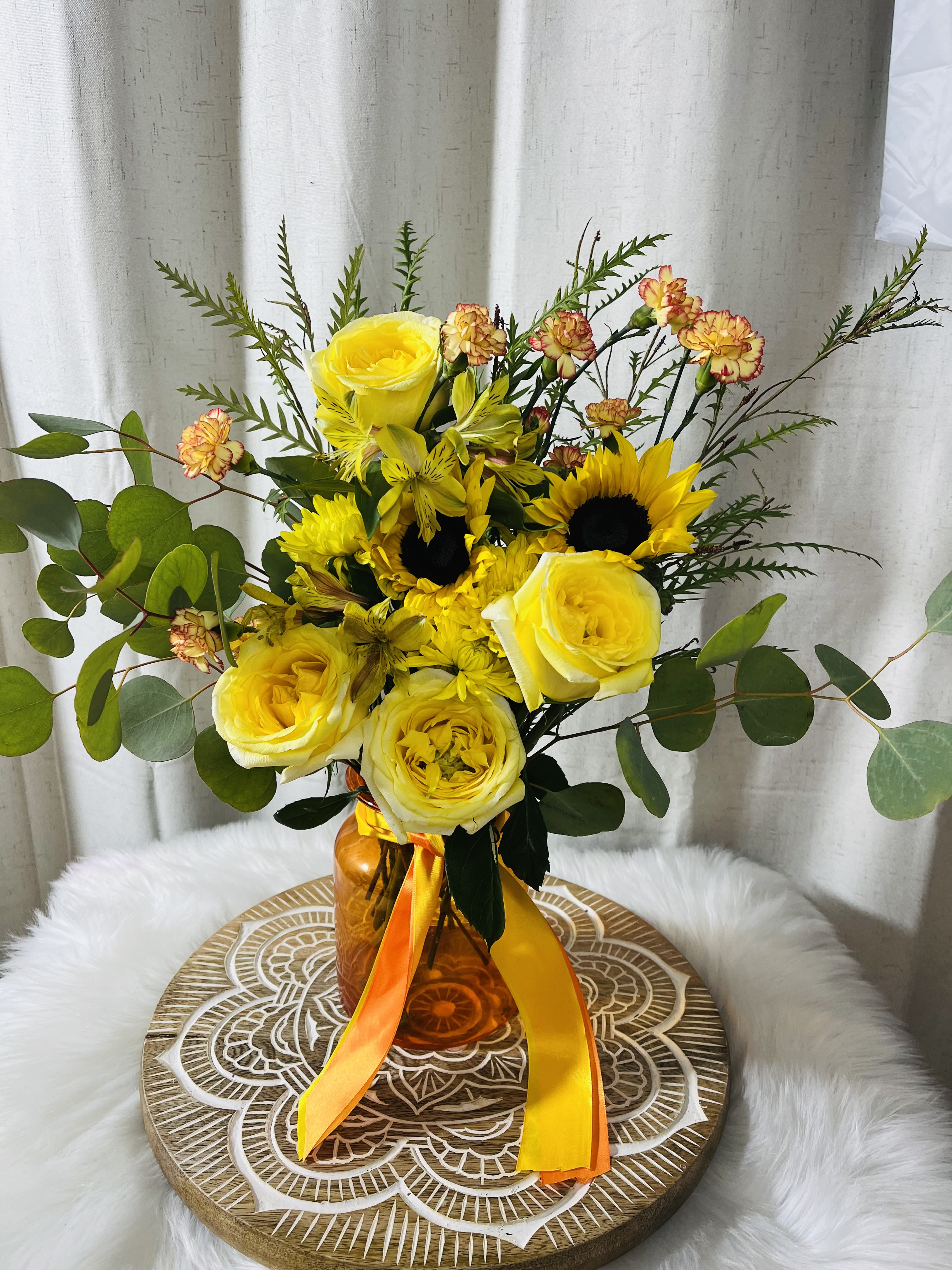 Yellow roses and sunflowers in an amber vase with orange ribbon