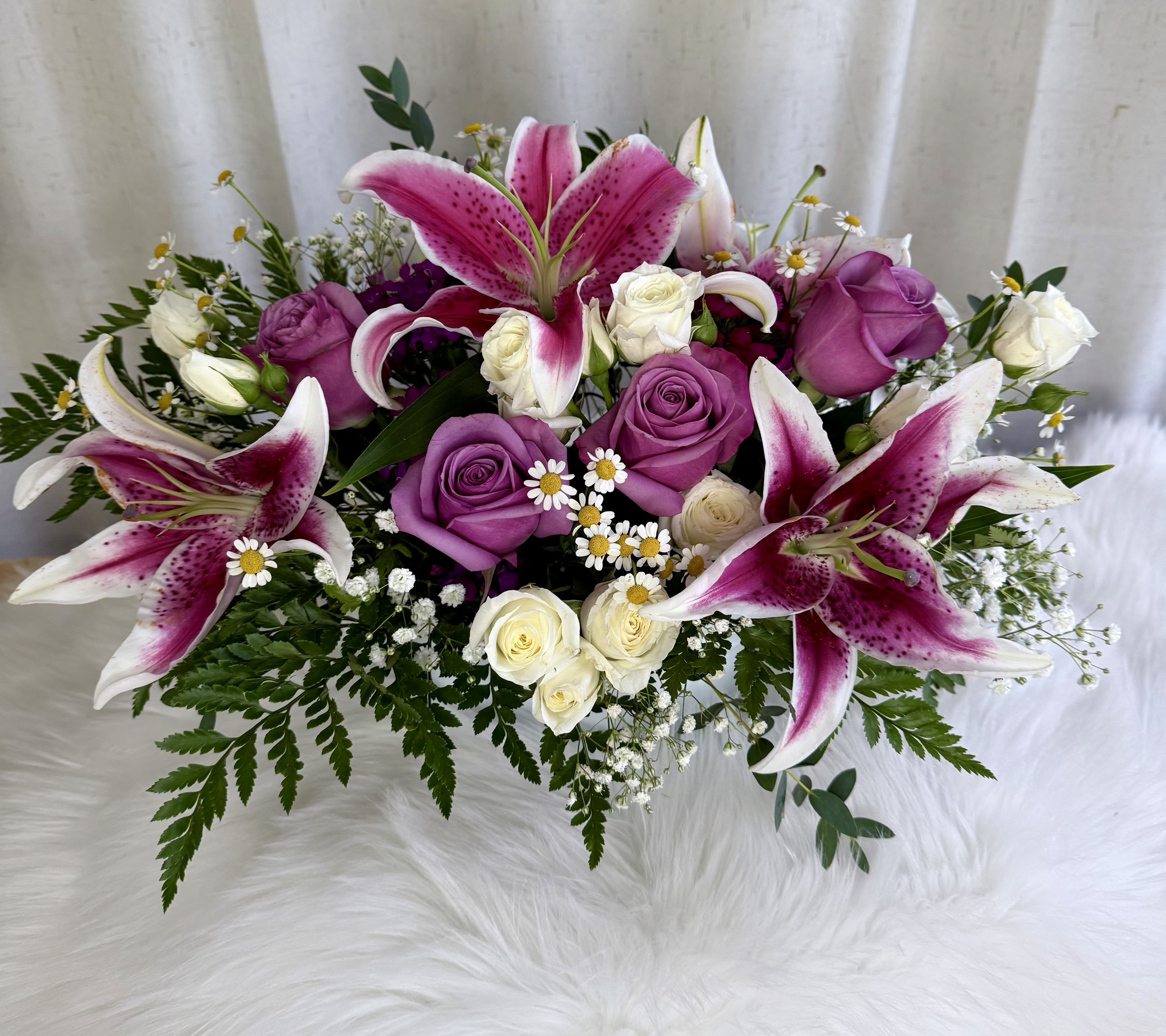 Pink lilies and purple roses arranged with small white flowers.
