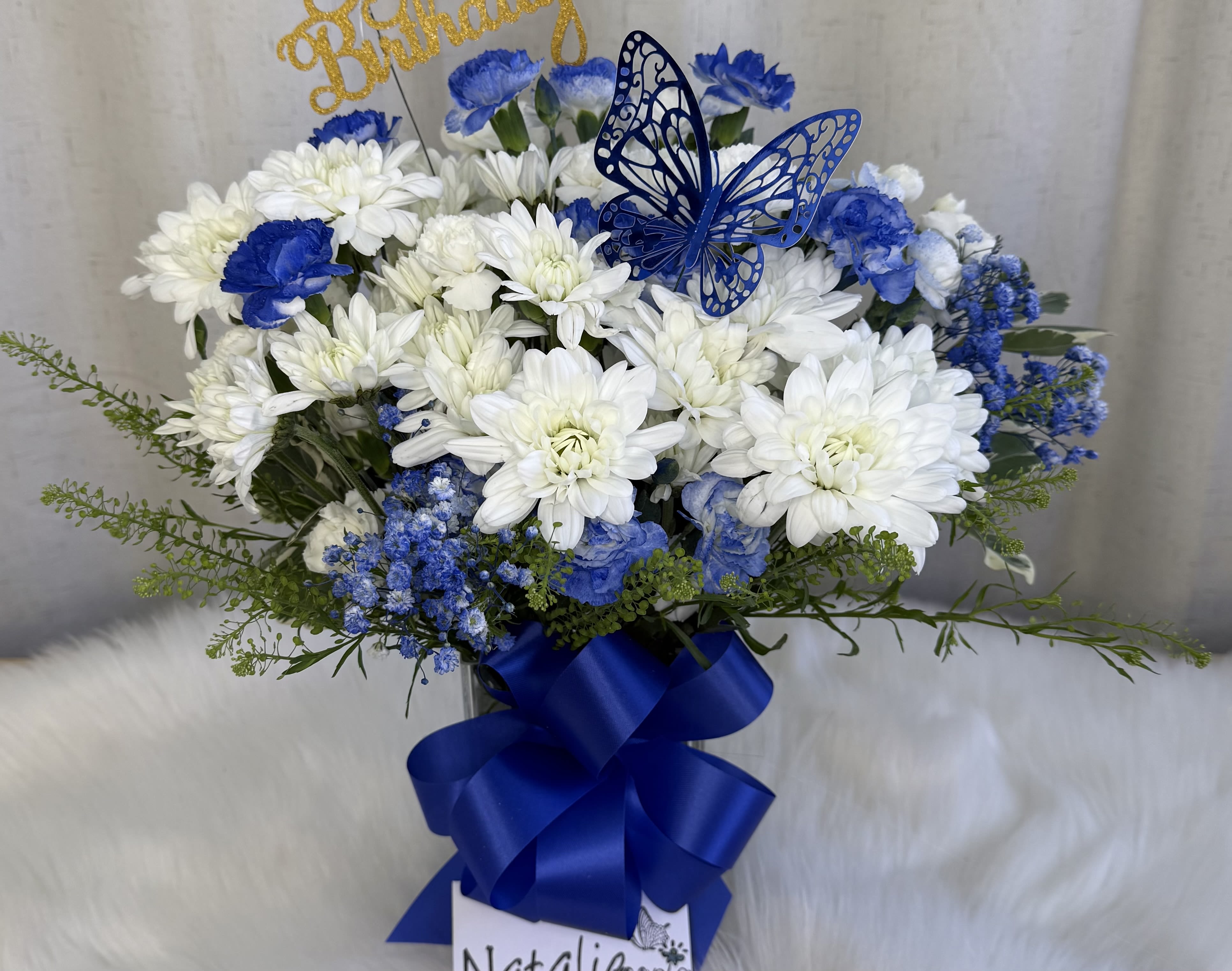 Blue and white flower arrangement with a butterfly topper and ribbon