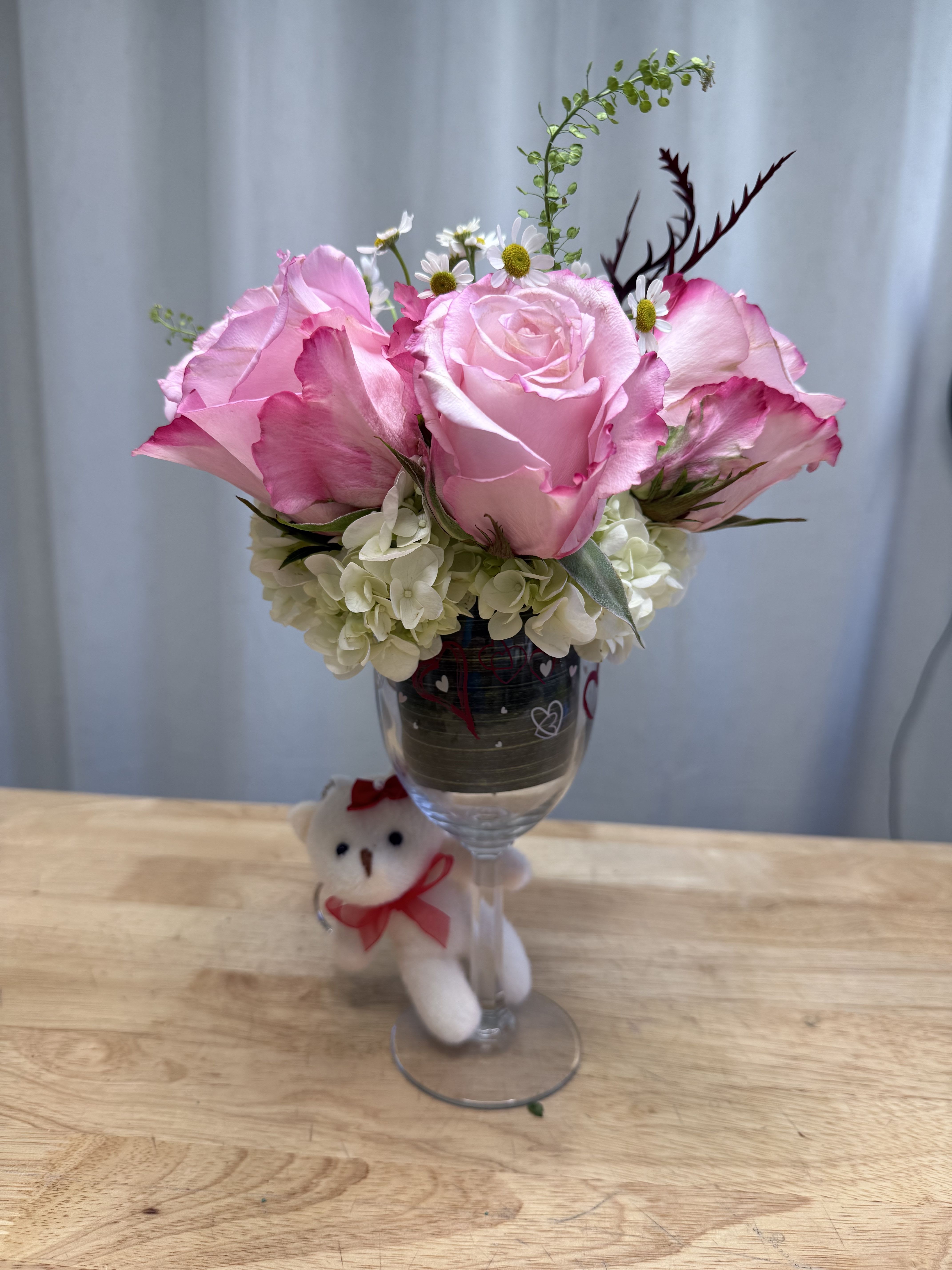 Pink roses and white hydrangeas in a wine glass with a small teddy bear