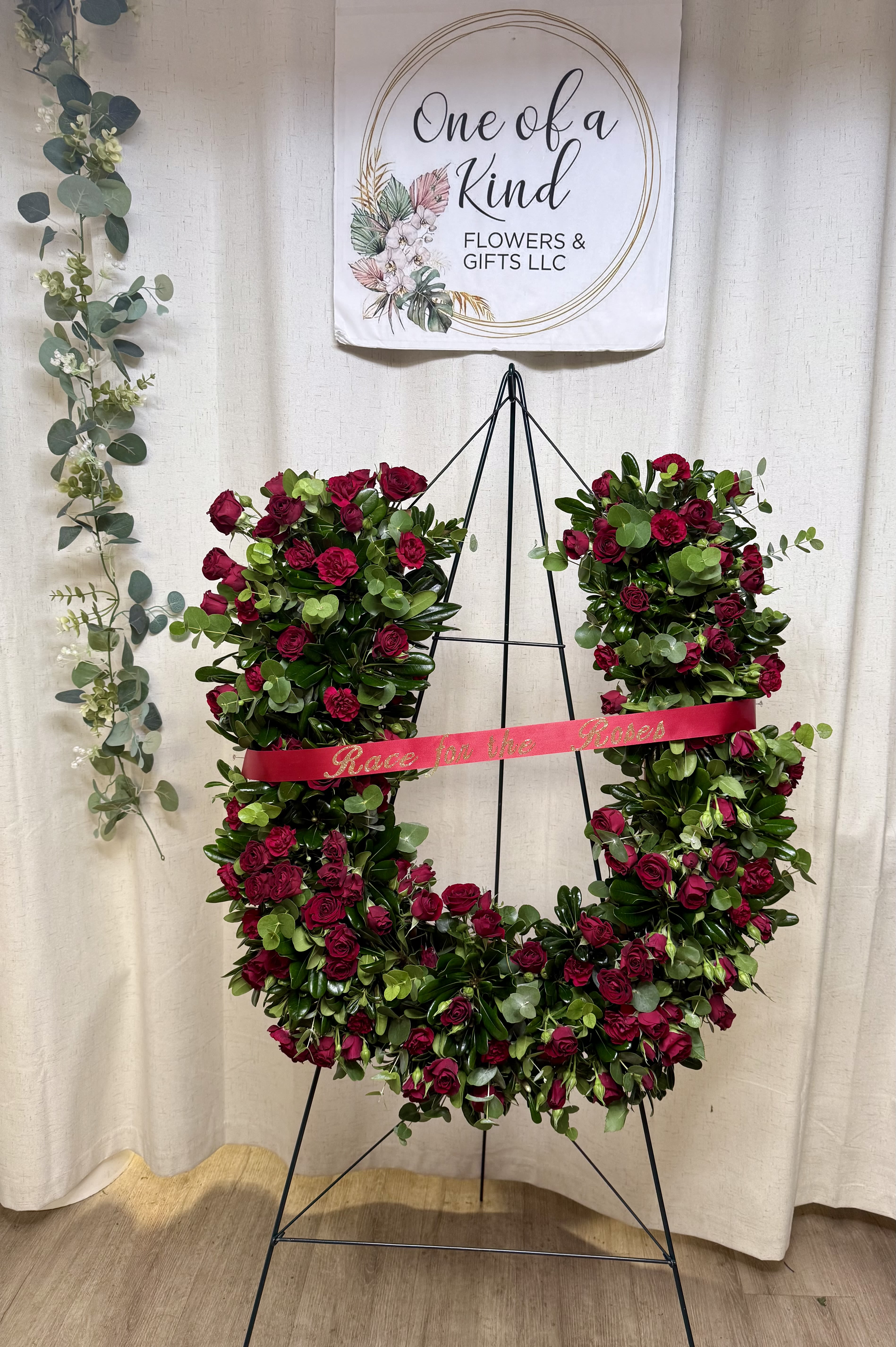 Horseshoe of Love &amp; Remembrance - A beautiful and meaningful horseshoe-shaped floral tribute, designed to honor a loved one with elegance and symbolism. This arrangement features fresh red roses paired with lush premium greenery, creating a full and sophisticated presentation.  The horseshoe shape represents luck, protection, and blessings, making it a heartfelt expression of love and remembrance. A decorative ribbon and bow add a refined finishing touch, enhancing its visual impact.  Perfect for funeral services or memorials, this tribute offers a timeless and graceful way to celebrate a life well lived.  Each piece is handcrafted and can be customized to your preferences.  Approximate dimensions: 2 feet tall  Includes personalized ribbon.   