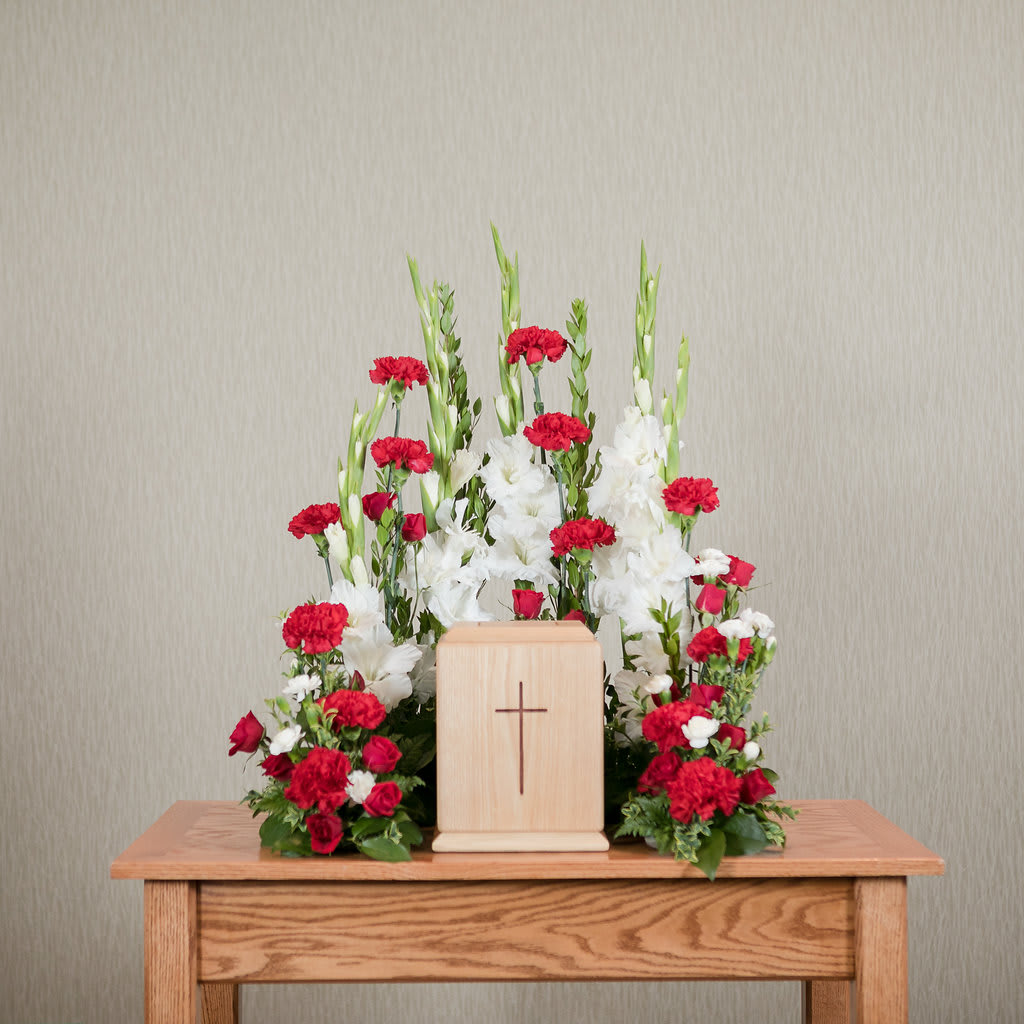 Red and white floral arrangement around a wooden cross urn.