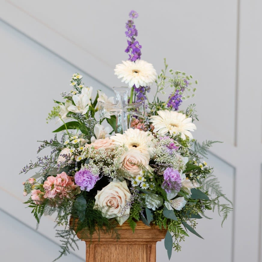 Mixed pastel flower arrangement in a clear glass vase on a wooden pedestal