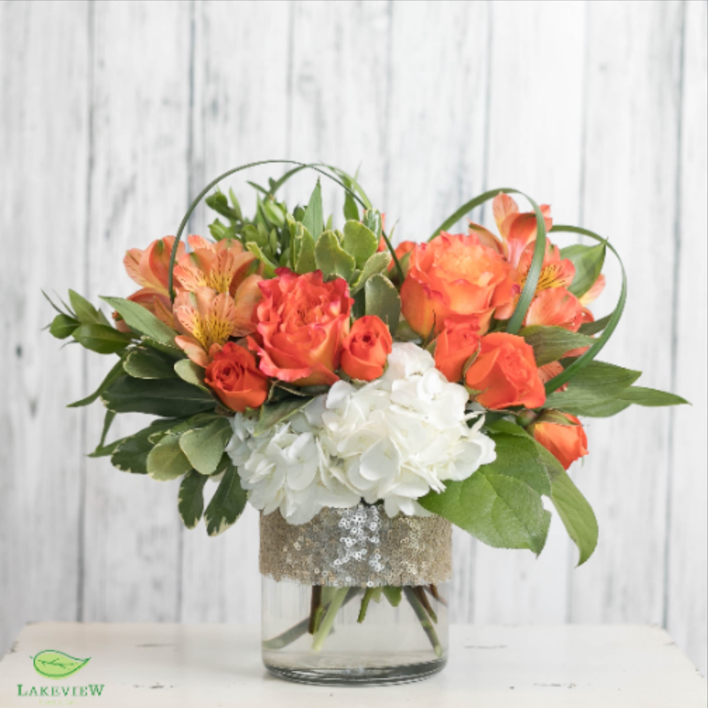 Orange roses and white hydrangeas in a glass vase with greenery