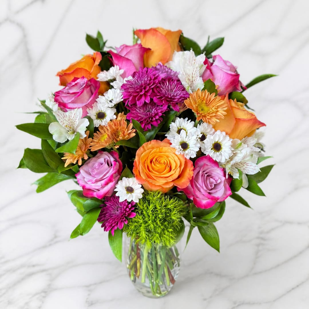 Mixed bouquet of pink and orange roses with white daisies in a glass vase