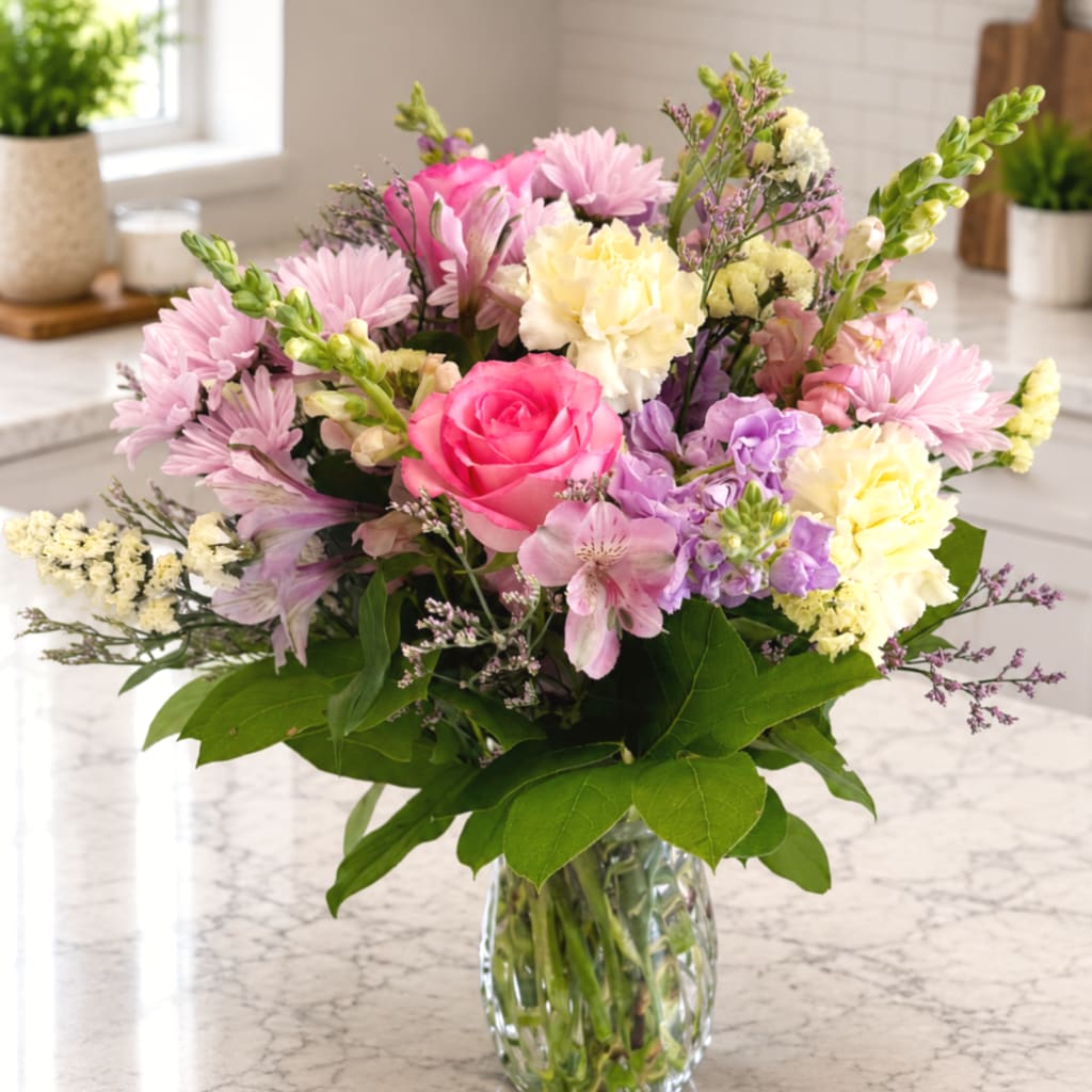Mixed pink, purple, and cream flowers in a clear glass vase