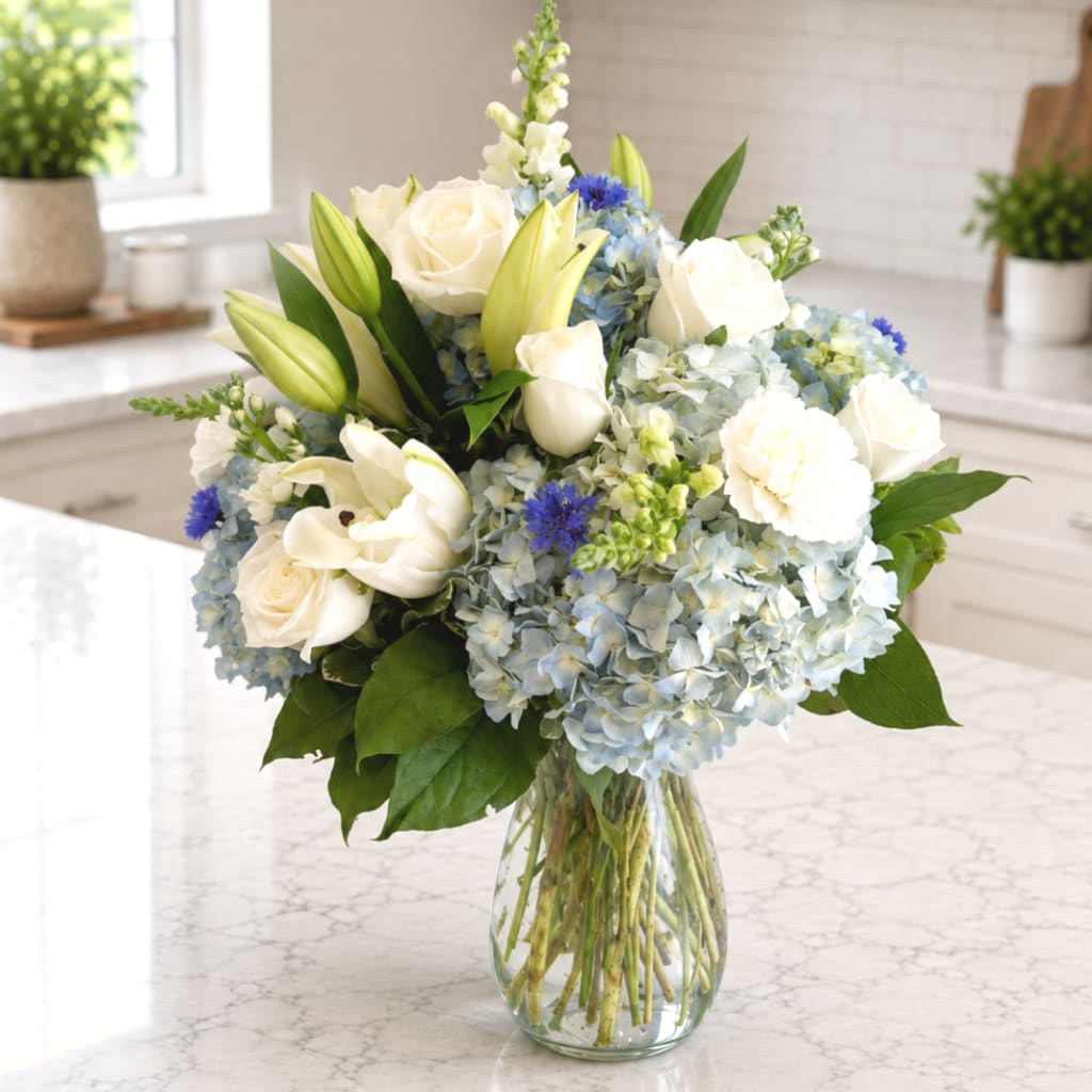White roses and lilies with blue hydrangeas in a glass vase