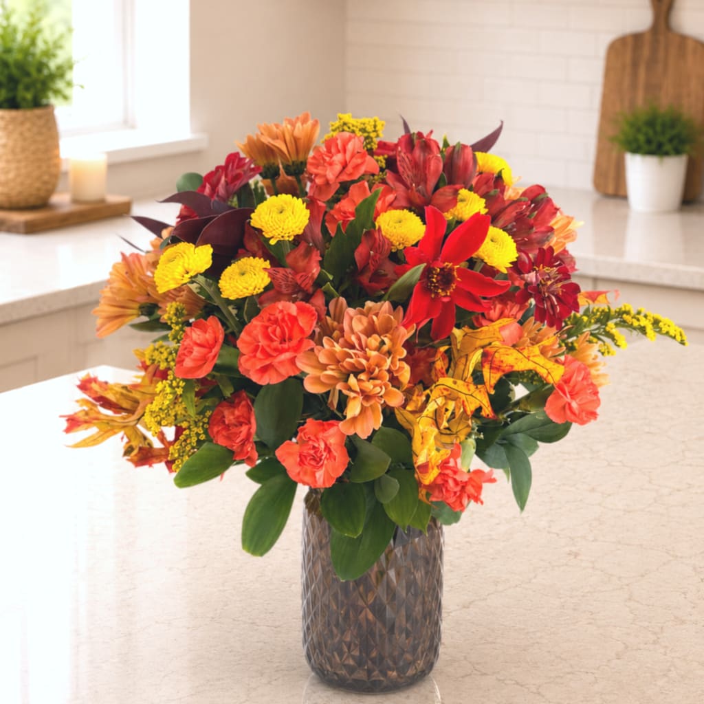 Mixed autumn bouquet in a textured glass vase with red, orange, and yellow blooms