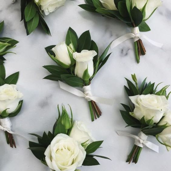 White rose boutonnieres with dark green leaves and white ribbon