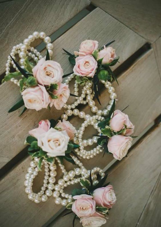 Pink rose corsages with pearl strands on a wooden surface