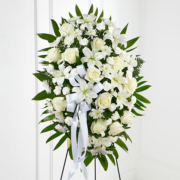 The  Exquisite Tribute Standing Spray - The Exquisite Tribute™ Standing Spray is an elegant display of sweet serenity. White roses Asiatic lilies chrysanthemums and mini carnations are artfully arranged amongst emerald palm fronds and lush greens. Accented by white satin ribbon and standing on a wire easel this standing spray is an outstanding way to honor the life of your loved one.