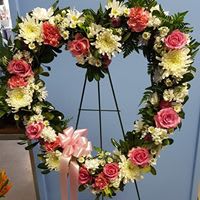 Heart-shaped floral wreath with pink roses and white flowers on a stand