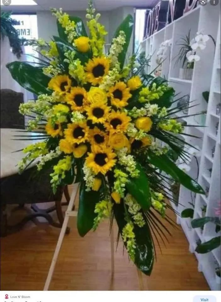 SUNNY SENTIMENTALSTANDING SPRAY - A STANDING EASEL WITH TROPICAL LEAFS, YELLOW ROSES, SNAPSDRAGONS AND SUNFLOWERS (STANDS AROUND 6' TALL)