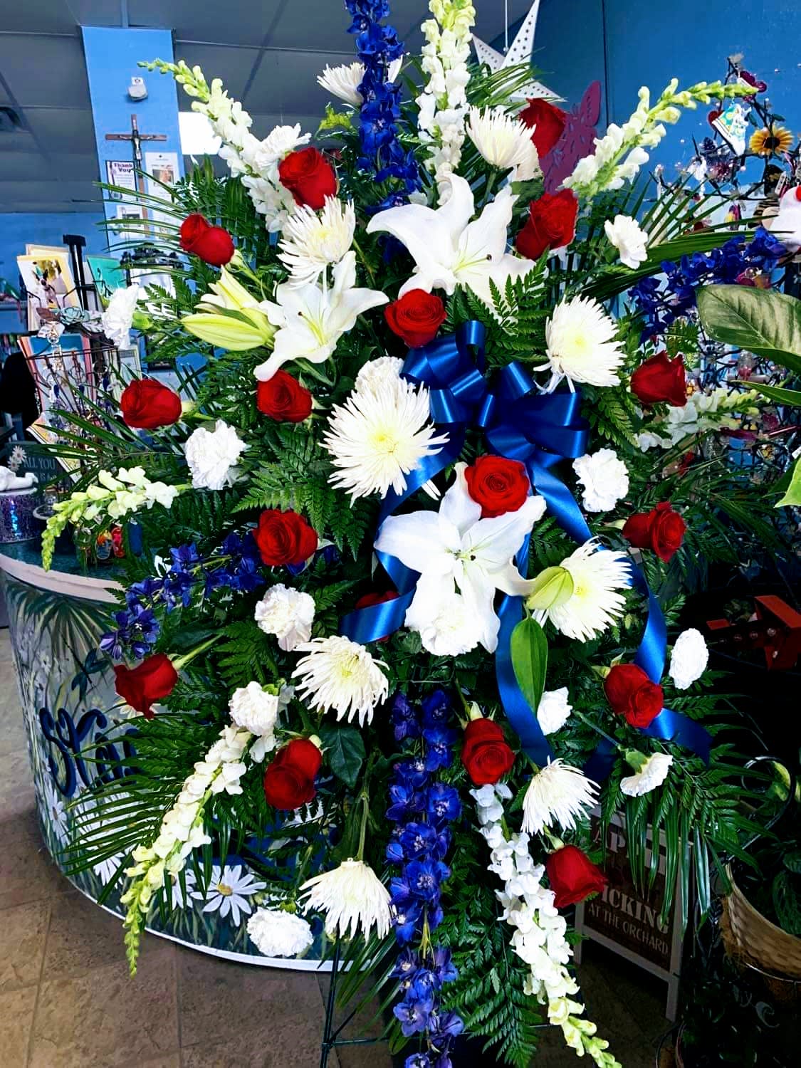 Large standing floral spray with red roses, white lilies, and blue ribbon
