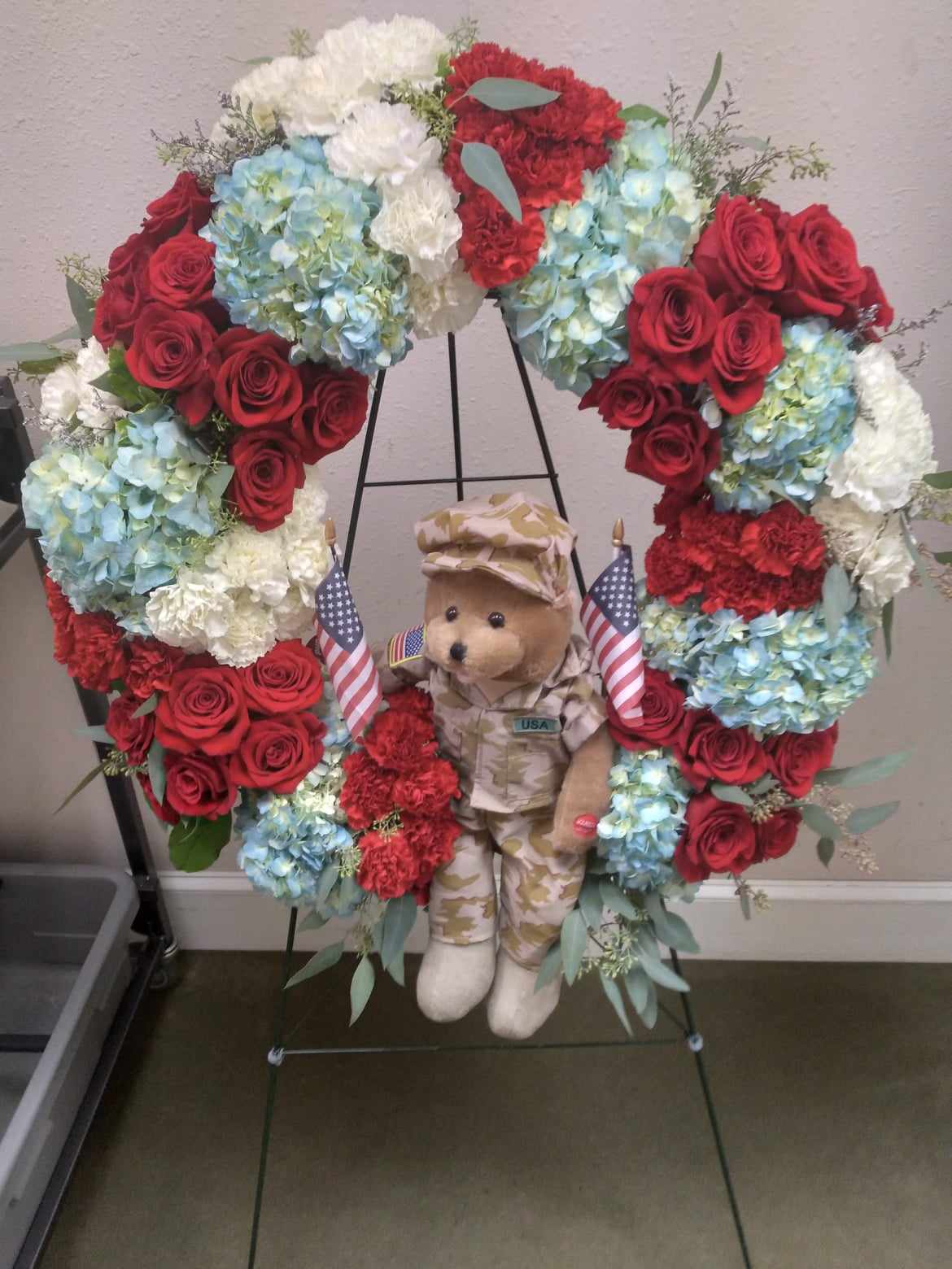 Heart-shaped floral wreath with roses, hydrangeas, and a teddy bear in military uniform