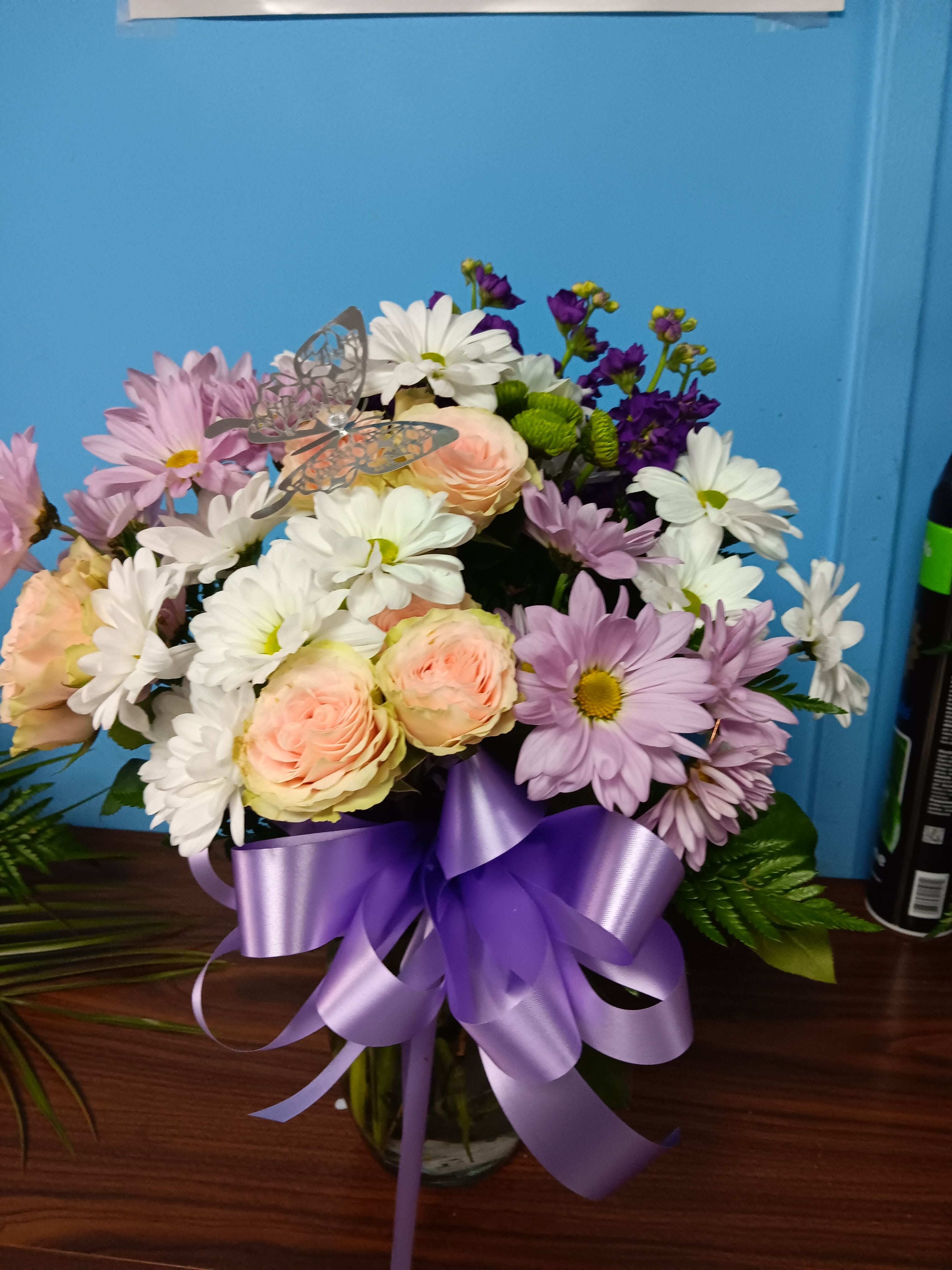 Mixed bouquet of pastel roses and daisies in a glass vase with a purple ribbon
