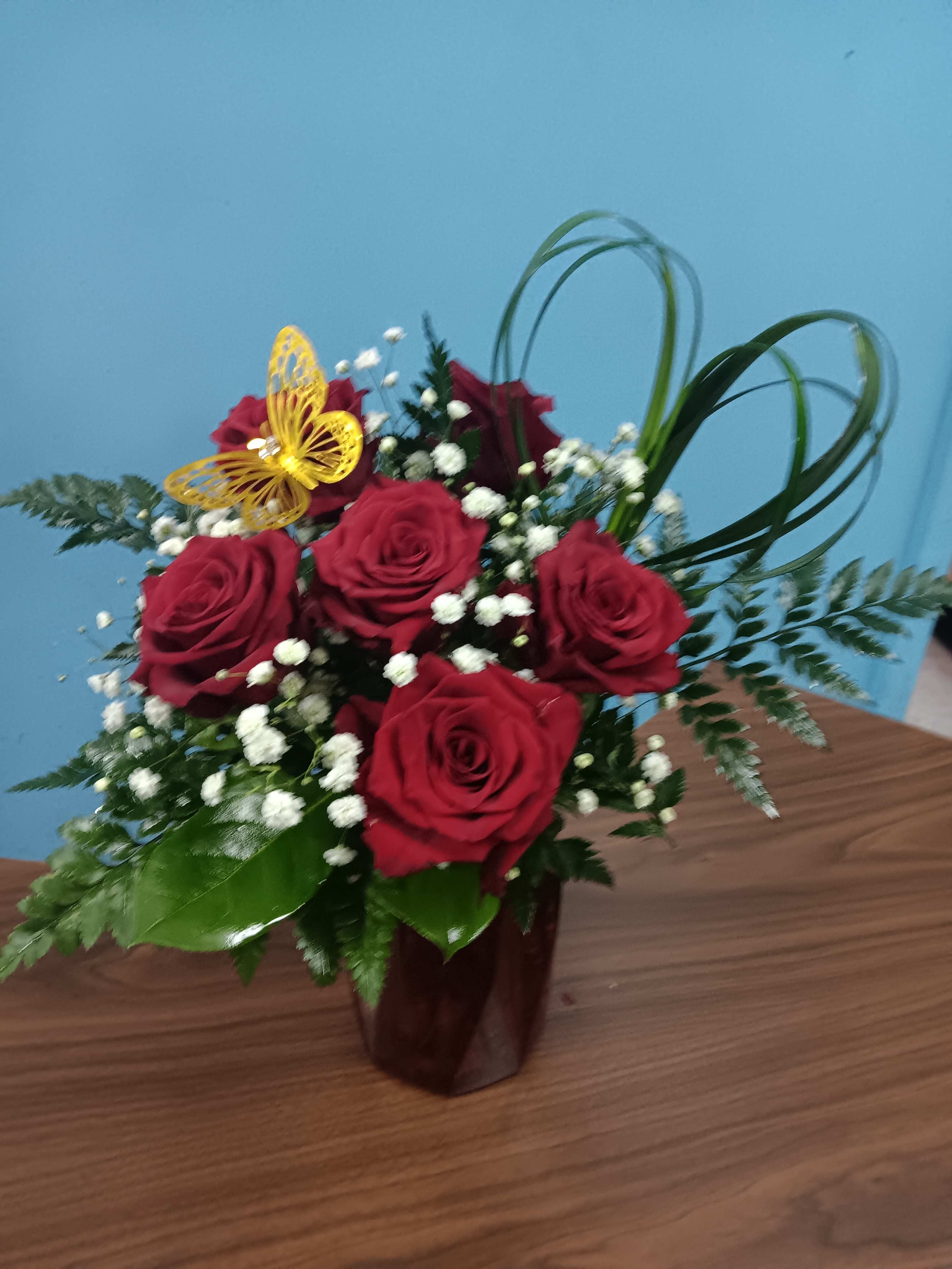 Red roses arranged in a dark vase with baby's breath and greenery