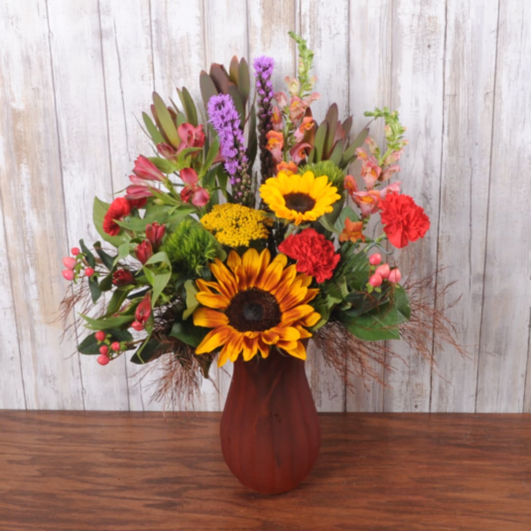 Mixed bouquet with sunflowers, carnations, and purple blooms in a red vase