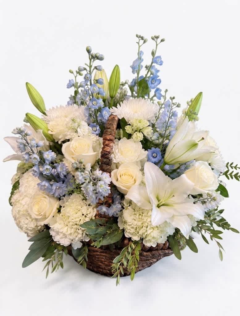 Basket arrangement of white lilies, roses, and blue flowers