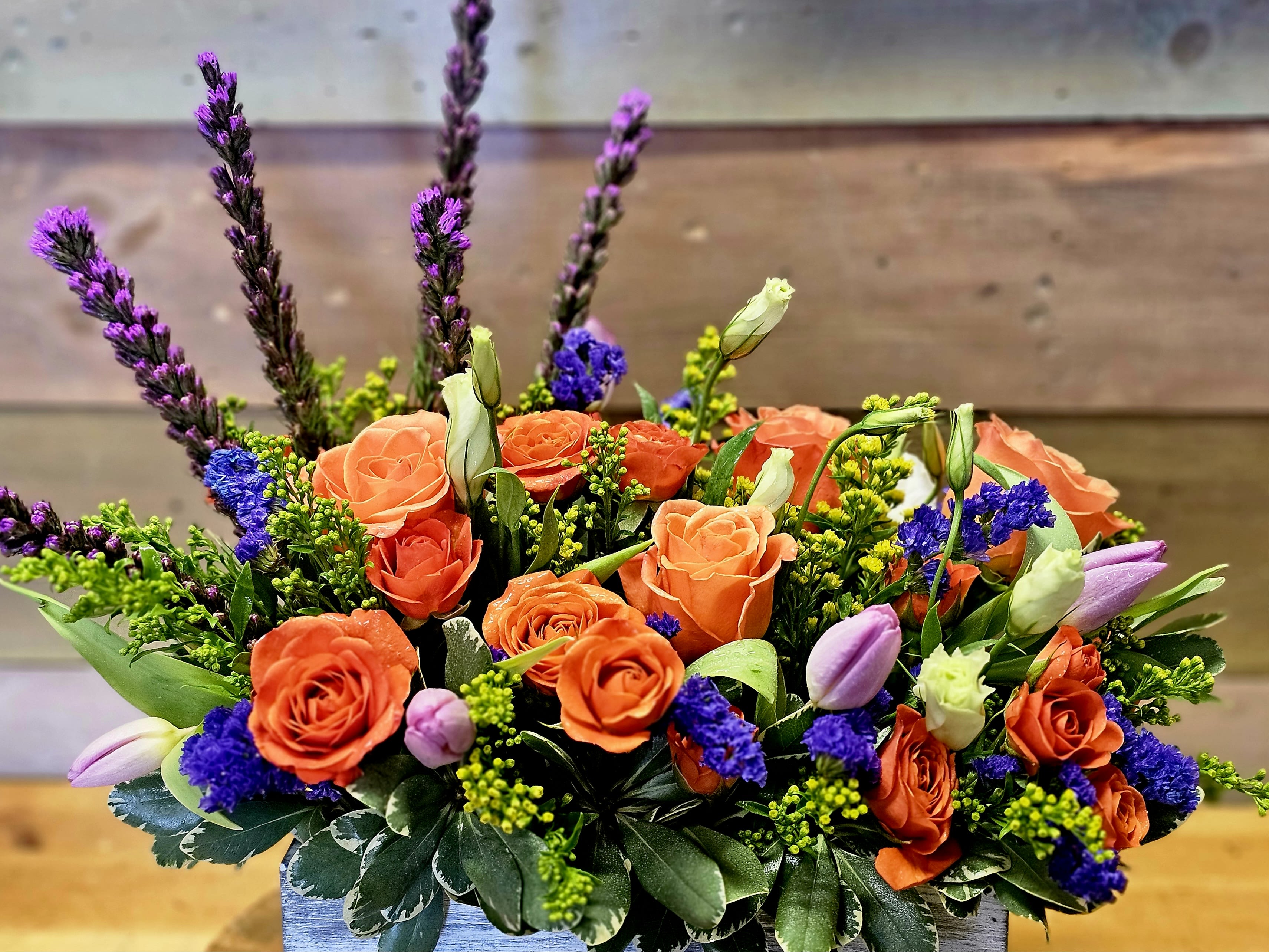 Orange roses and purple flowers in a low rectangular arrangement