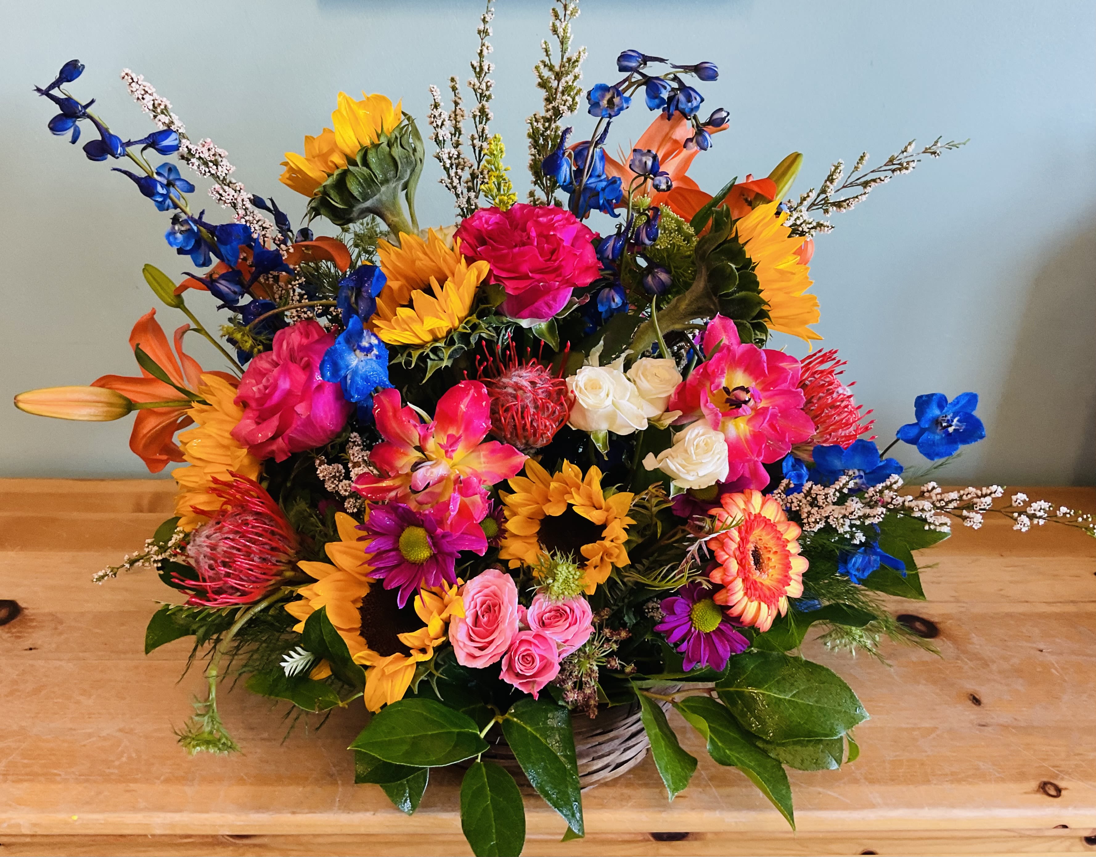 Celebration Day - For a truly wonderful celebration, choose this big, bold and colorful flower arrangement of assorted blossoms. It’s like summertime in a basket! Arrangement shown is Deluxe.  Flowers may vary from photo based on availability 