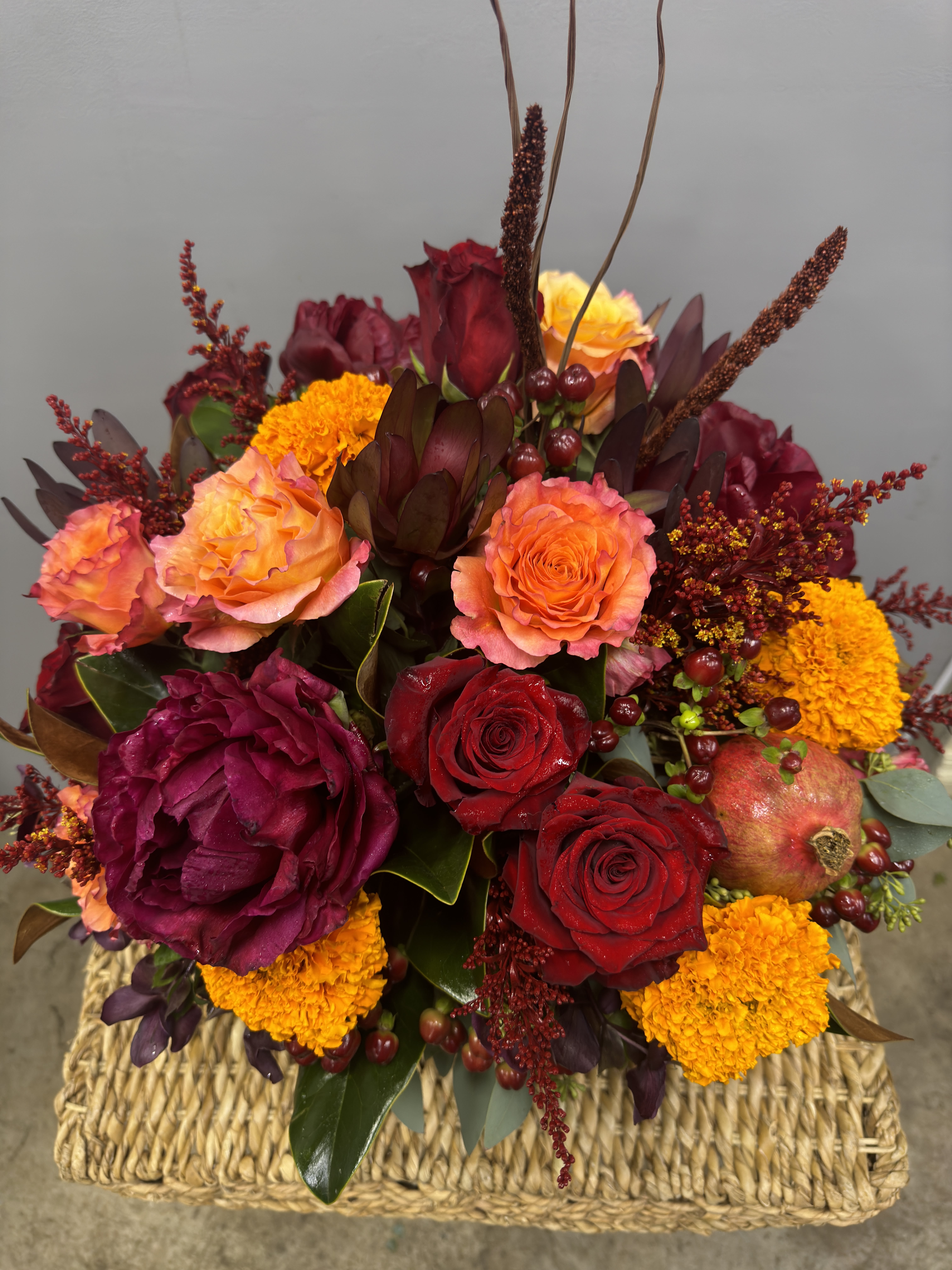 Mixed bouquet of red and orange roses with marigolds in a woven basket