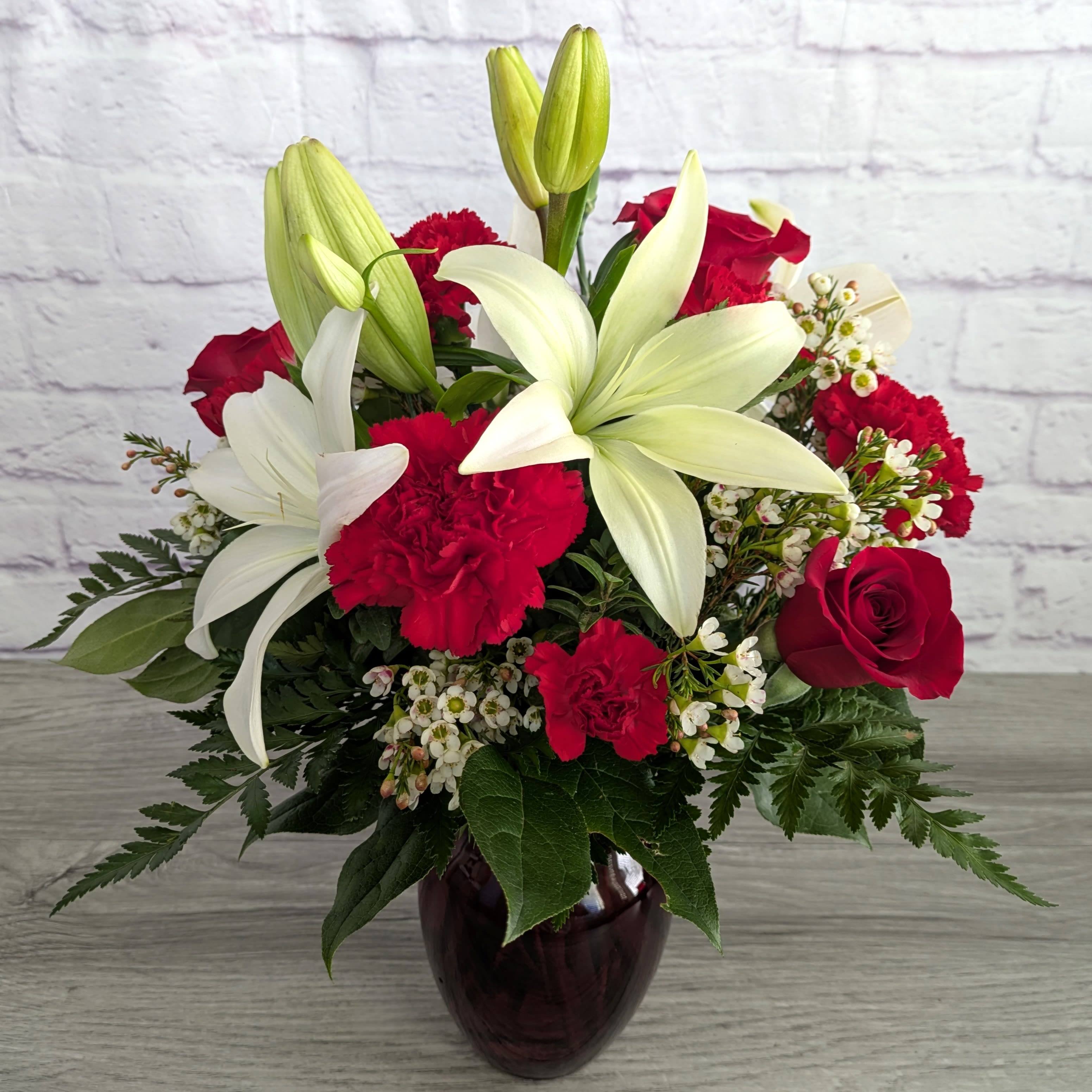 Bouquet of white lilies, red roses, and red carnations in a dark glass vase
