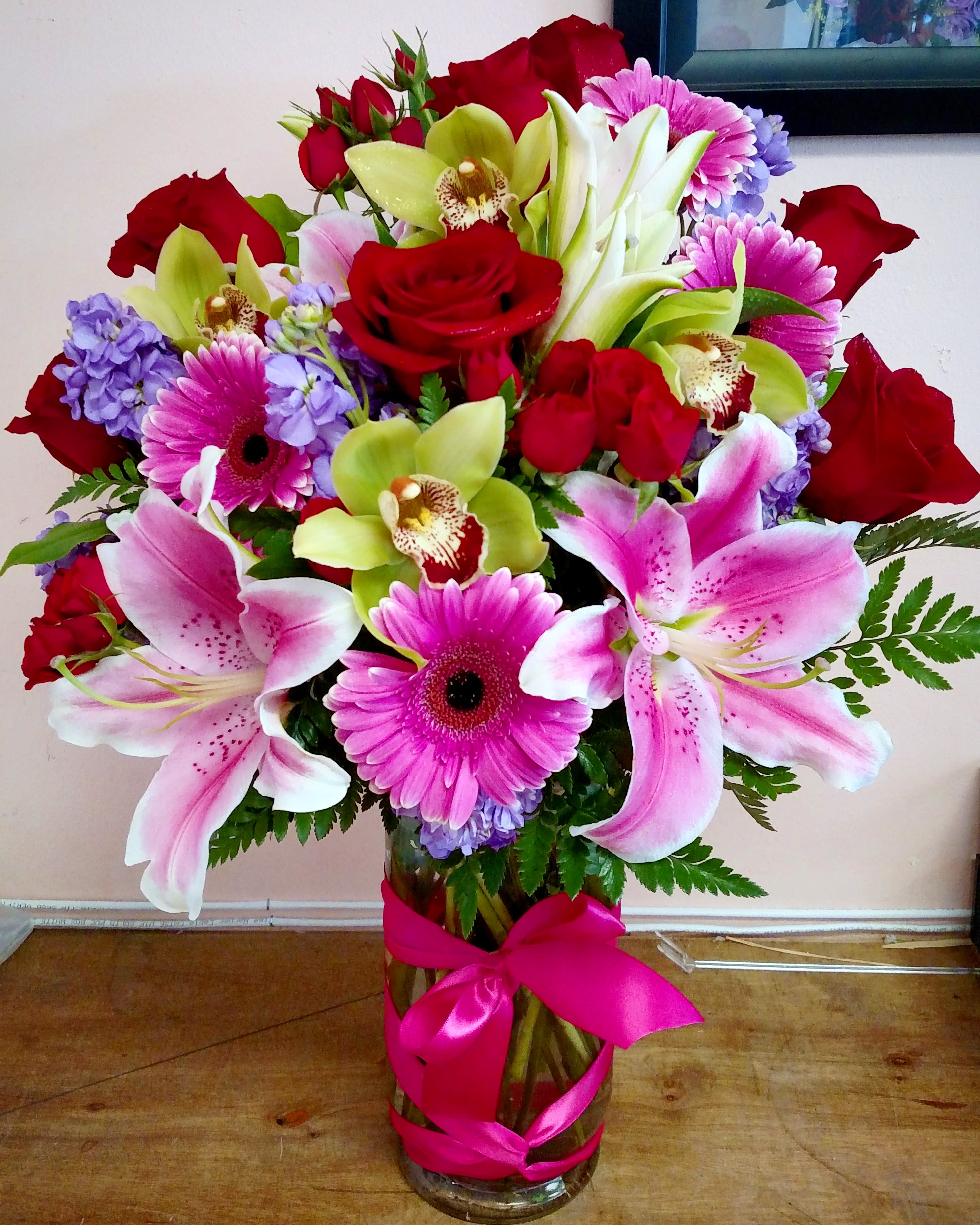 Bouquet of pink lilies, red roses, and purple flowers in a glass vase