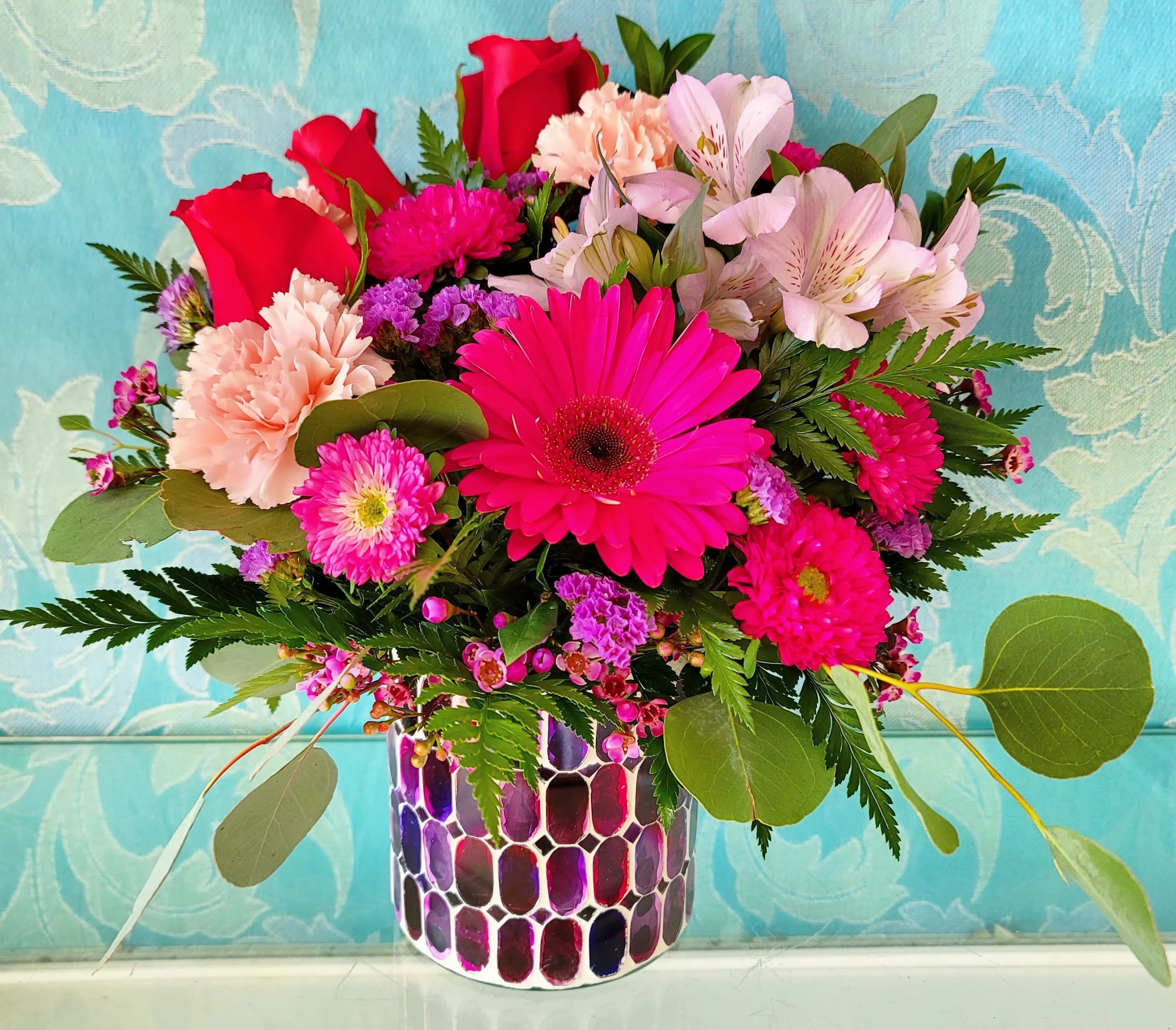 Mixed bouquet of pink and red flowers in a patterned vase