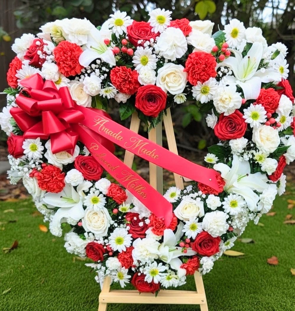 Heart-shaped floral wreath with red and white flowers and a pink ribbon