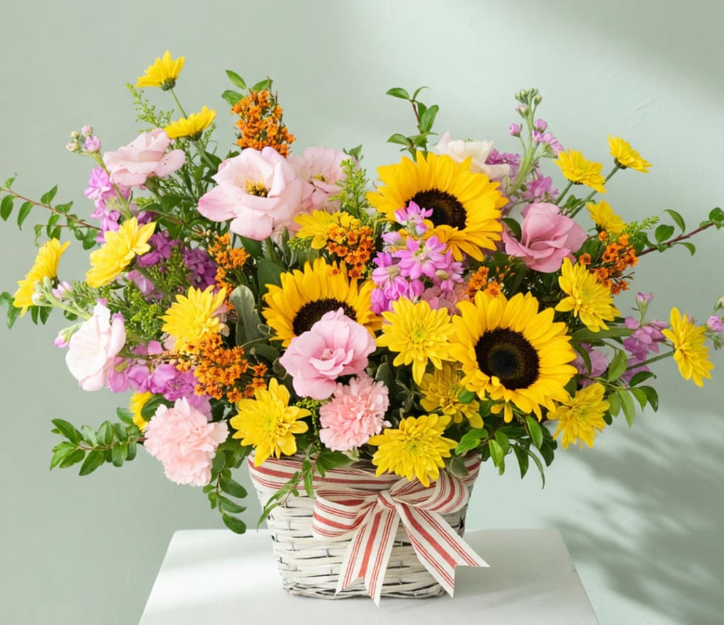 Basket arrangement with sunflowers, pink blooms, and a striped ribbon