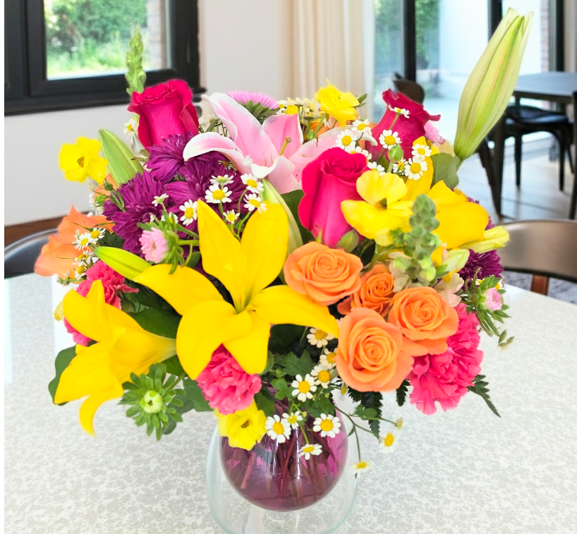 Colorful mixed bouquet in a glass vase with lilies, roses, and daisies