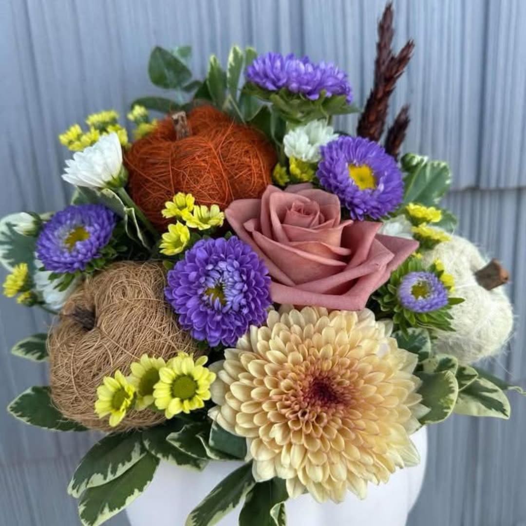 Mixed bouquet with a pink rose, purple daisies, and decorative balls in a white vase