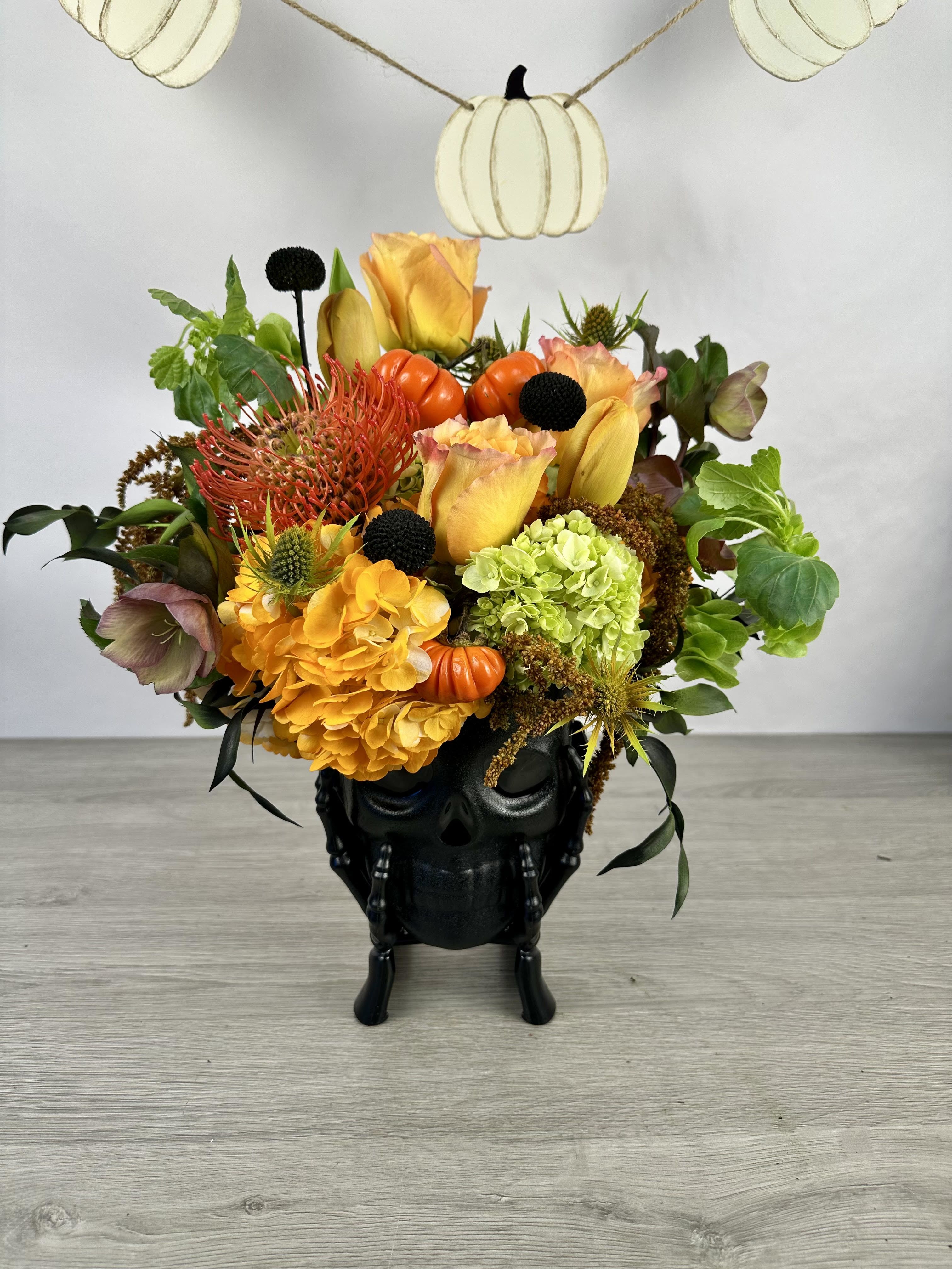 Halloween floral arrangement in a black skull vase with pumpkins